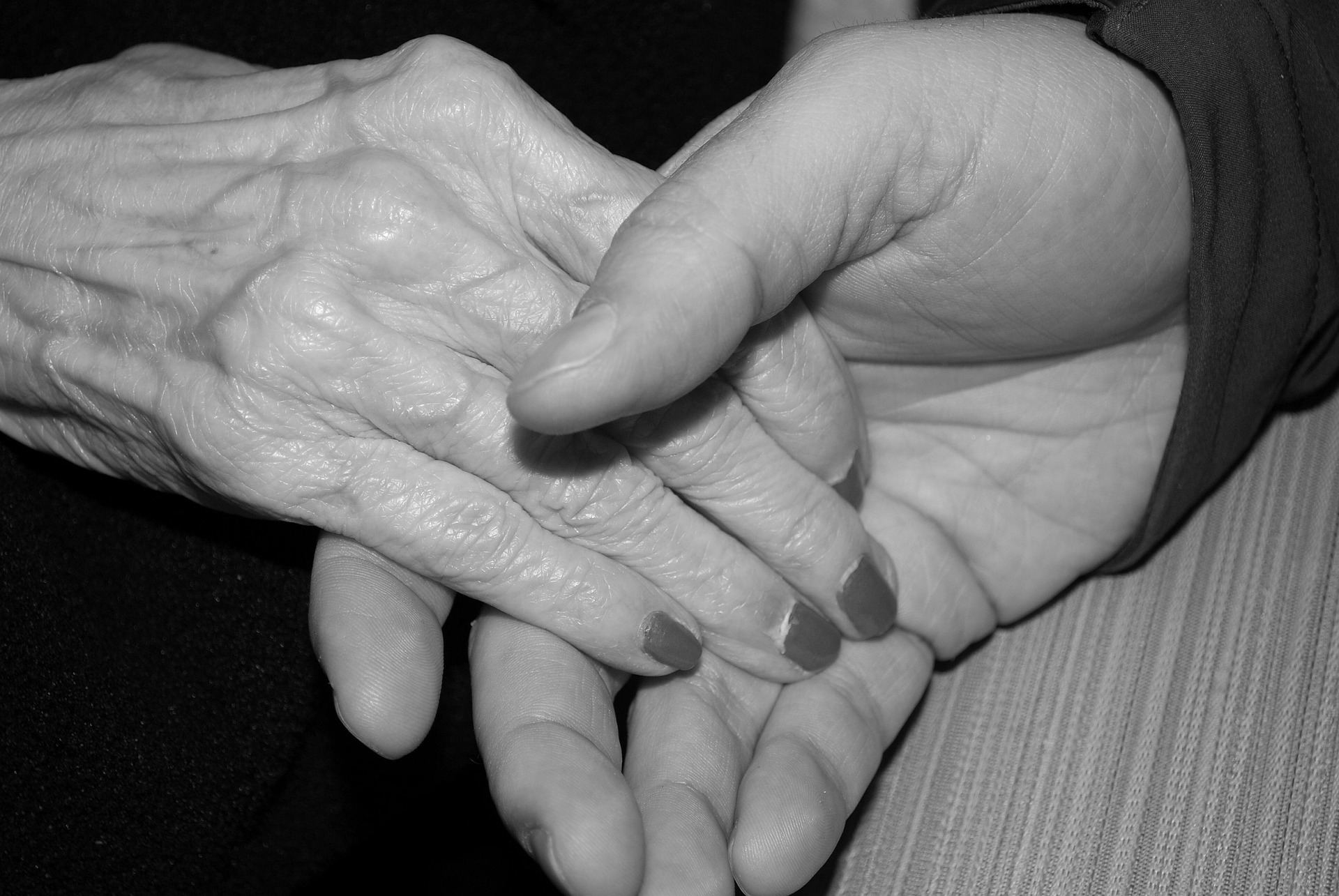 Close-up grayscale shot of a young man holding an older woman's hand | Source: Pixabay