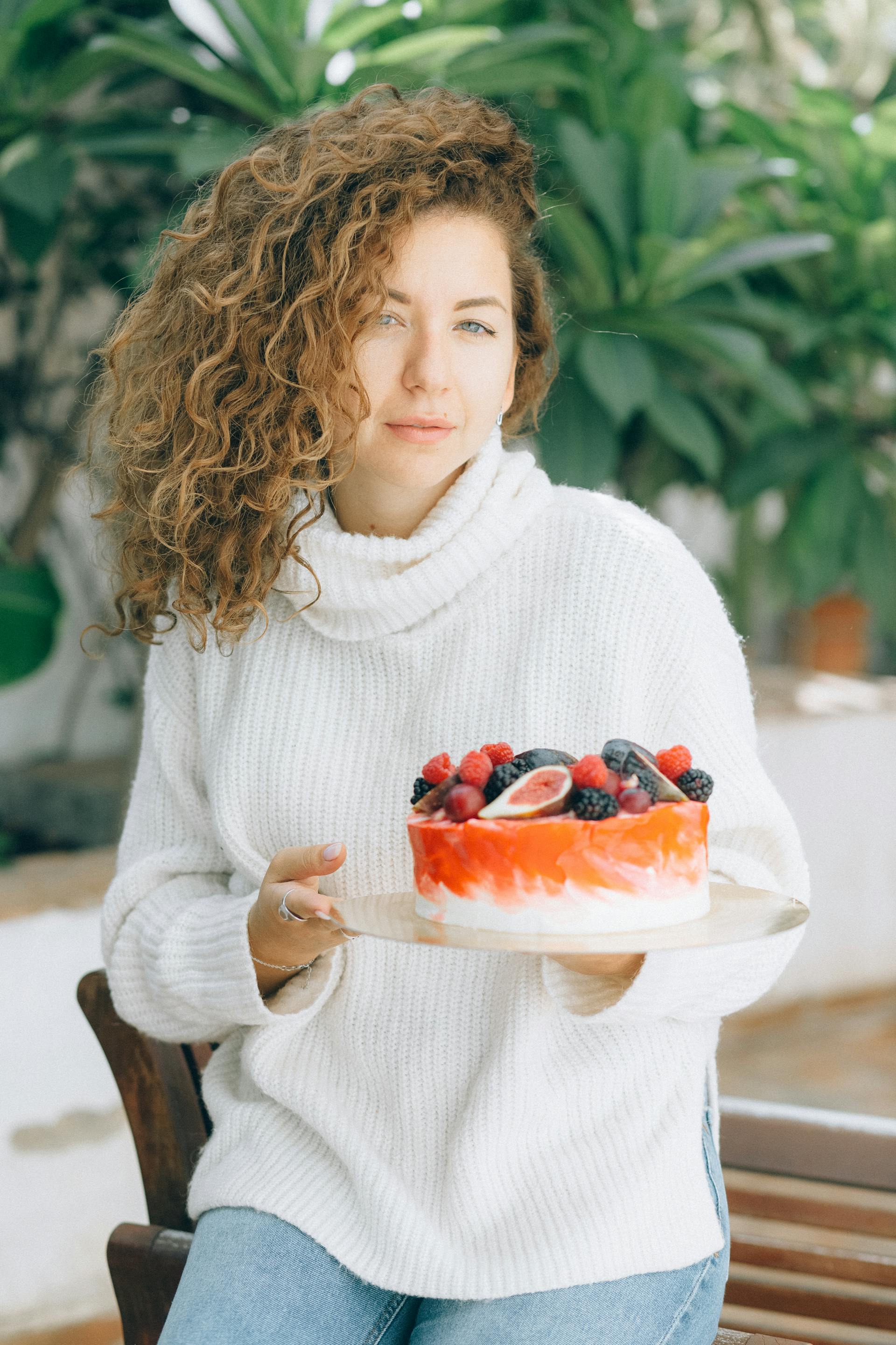 A woman in a white sweater holding a cheesecake topped with fruits | Source: Pexels