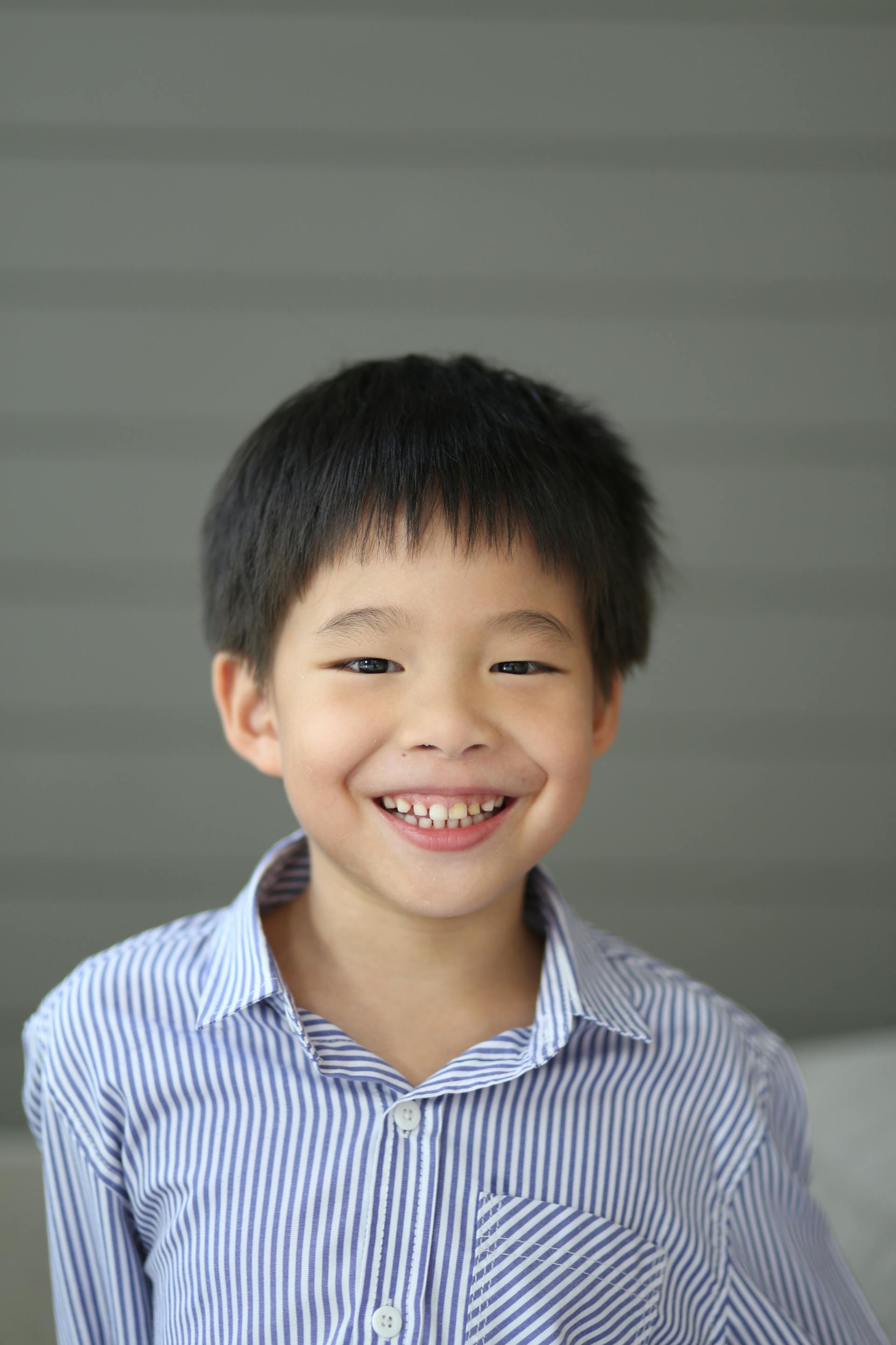 A young boy with short black hair smiling widely while wearing a striped shirt | Source: Pexels