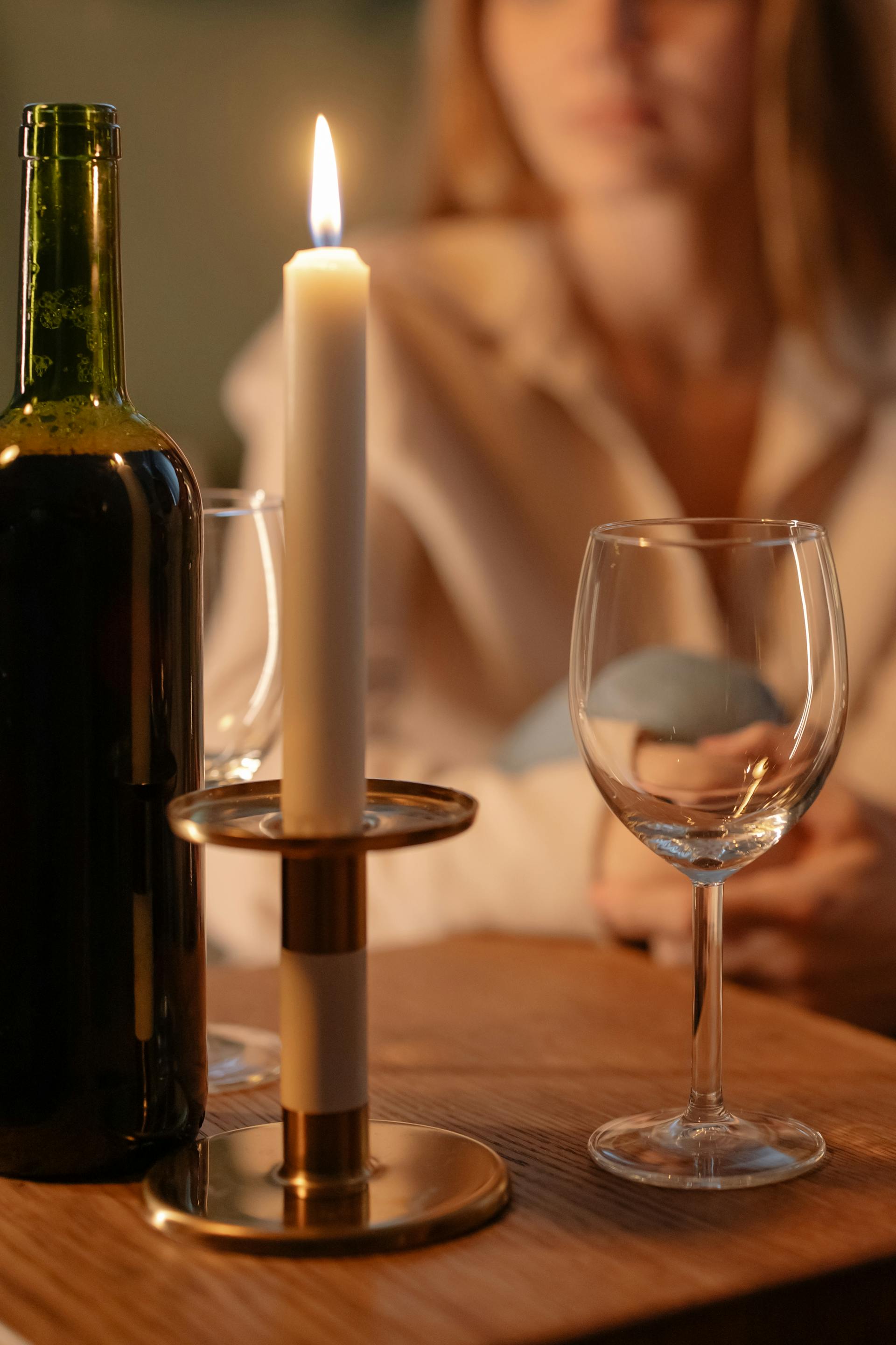 A lit candle and a wine bottle on a table in front of a woman | Source: Pexels