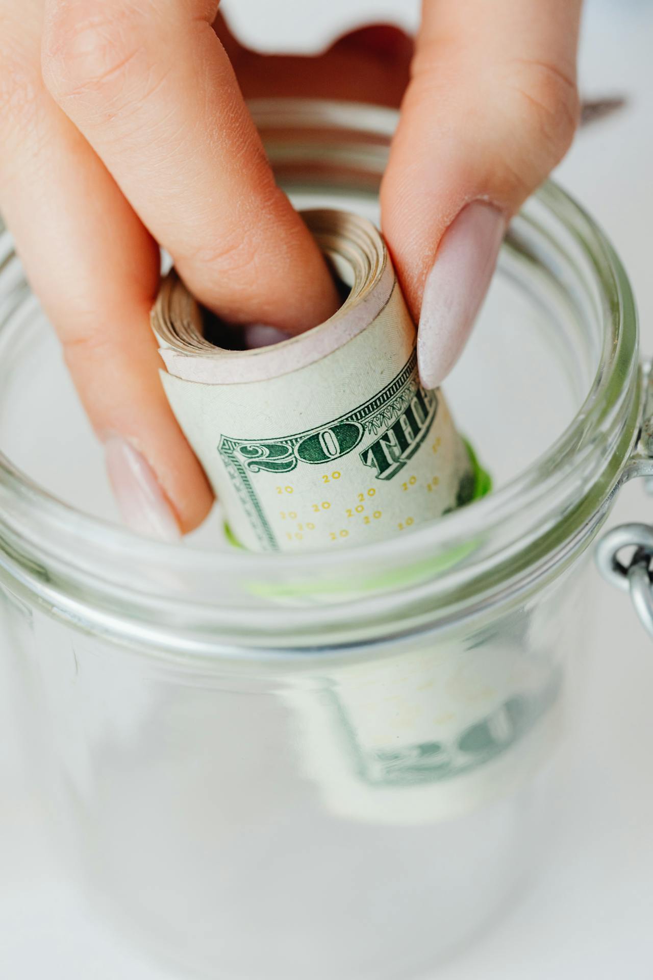 A woman putting rolled banknotes in a glass jar | Source: Pexels