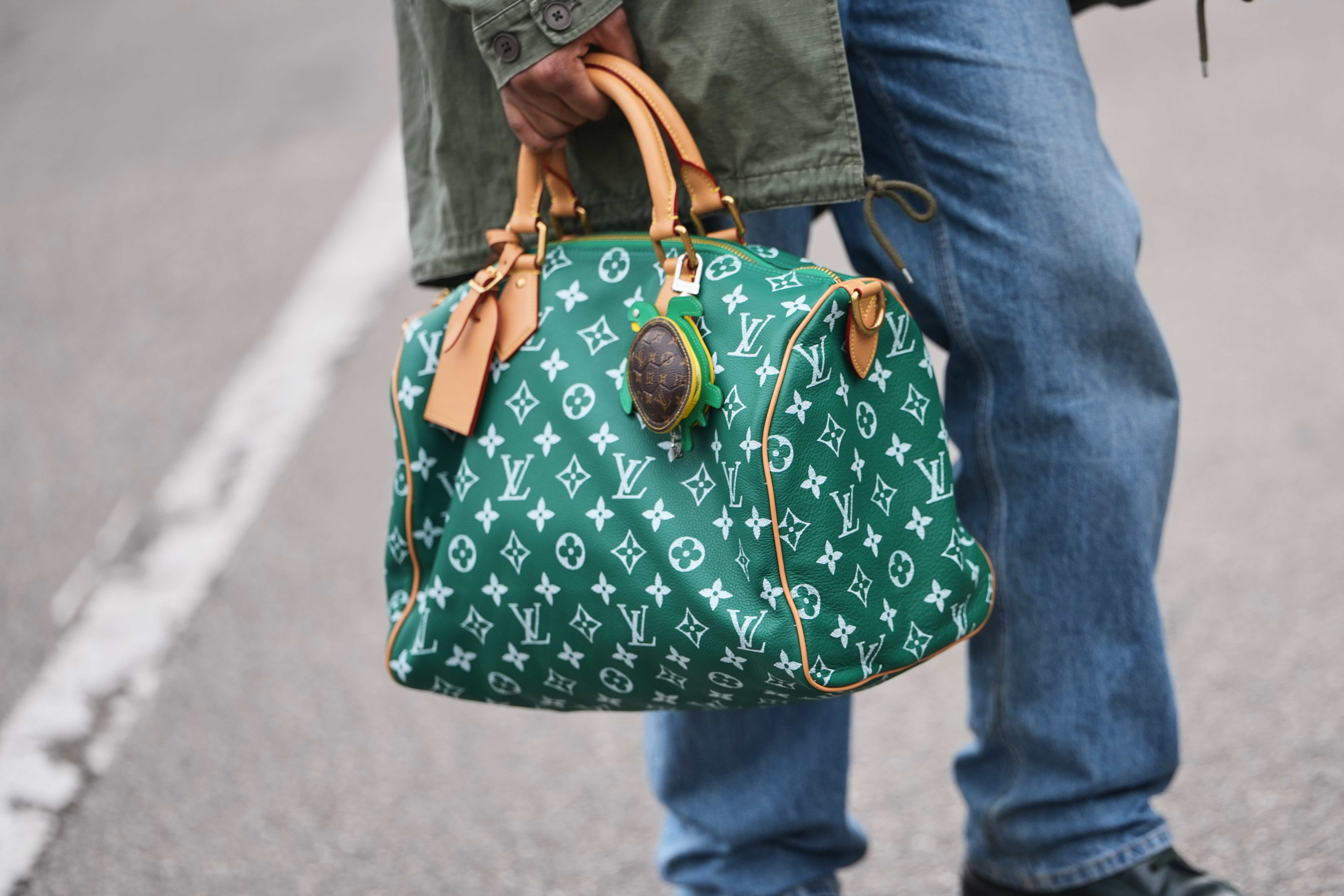 A guest wears a green with white LV monogram print pattern in coated canvas Speedy handbag from Louis Vuitton during Milan Fashion Week - Womenswear Fall/Winter 2026/2027, on February 24, 2026 in Milan, Italy. | Source: Getty Images