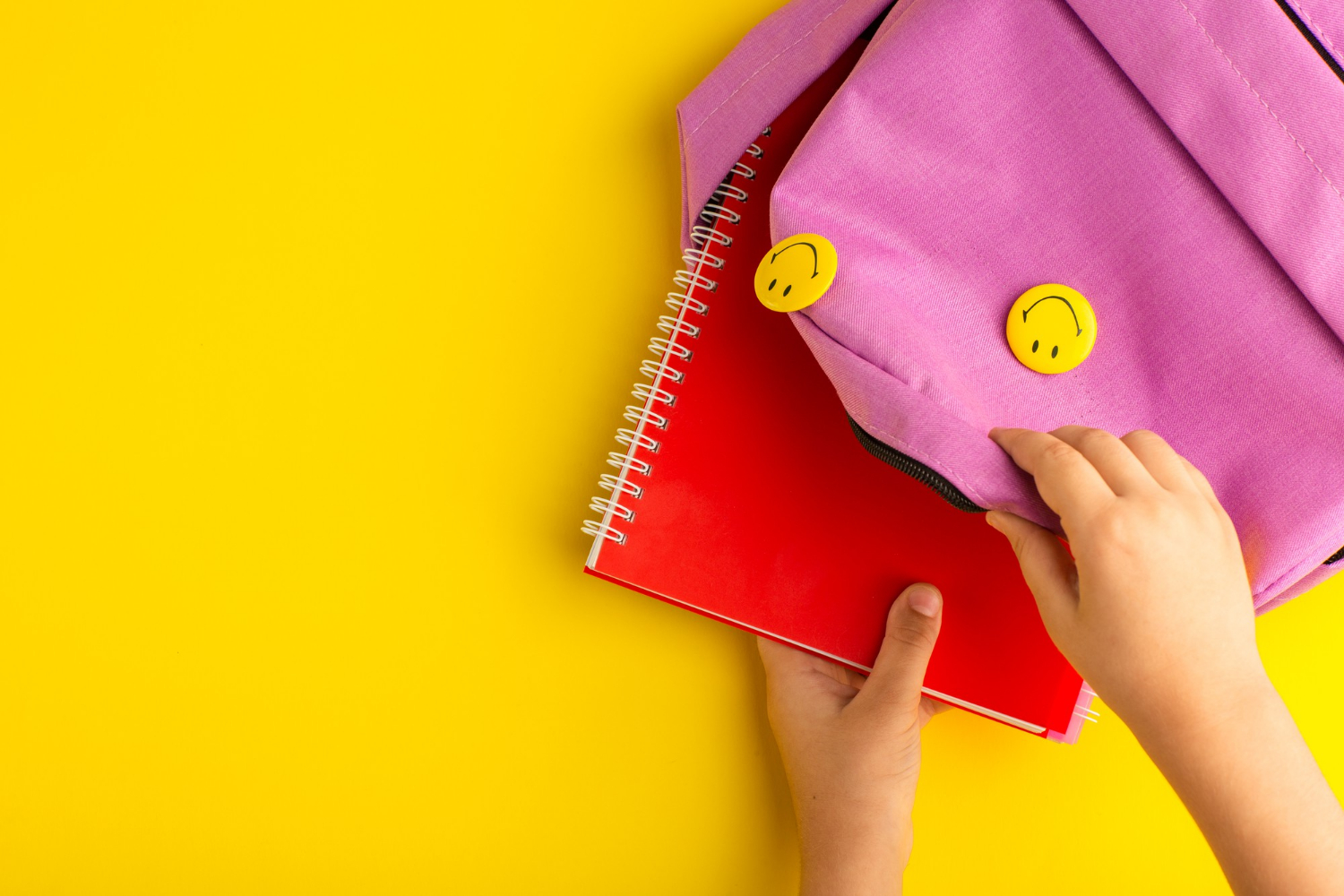 Close-up shot of a child putting a notebook inside a pink bag | Source: Freepik