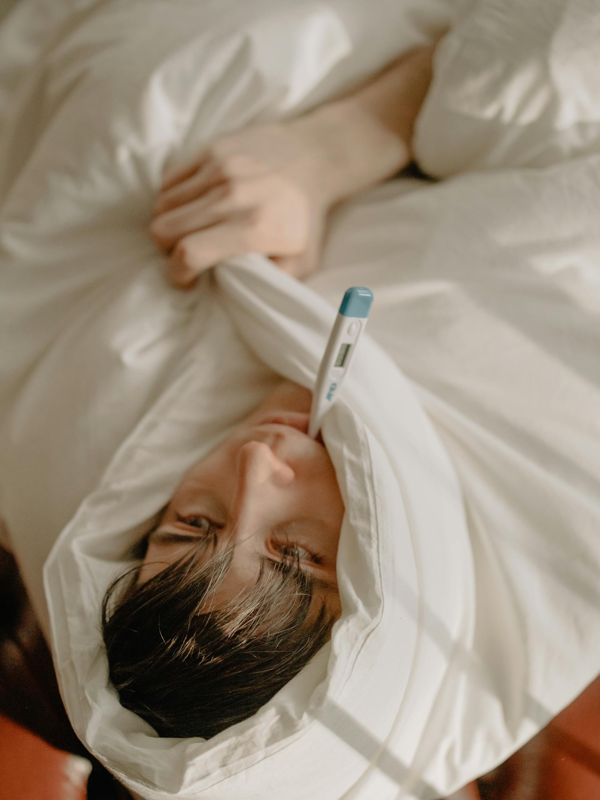 A man suffering from fever and flu lying in bed with a thermometer in his mouth | Source: Pexels