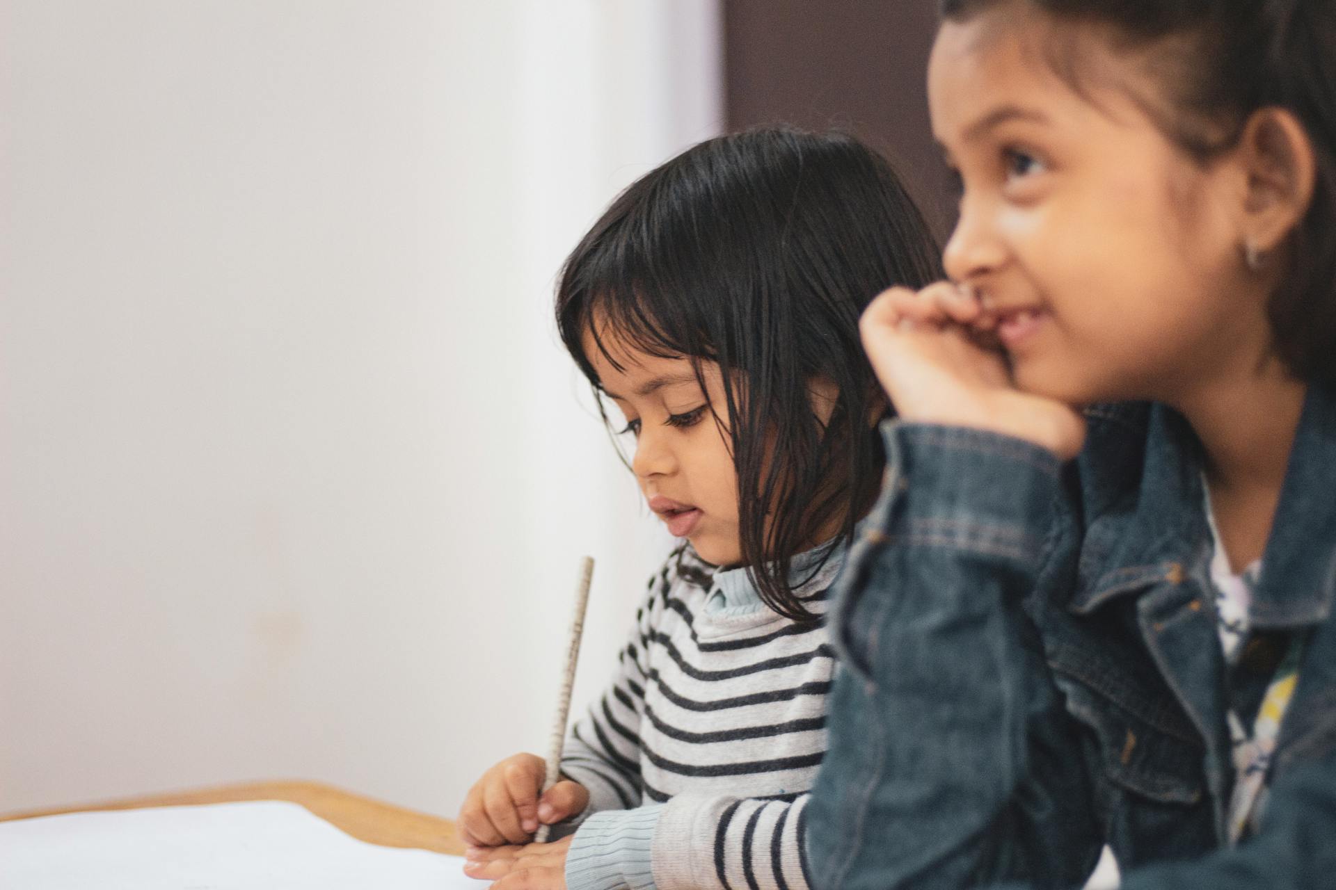 Girls seated at a desk, one girl writing on paper | Source: Pexels