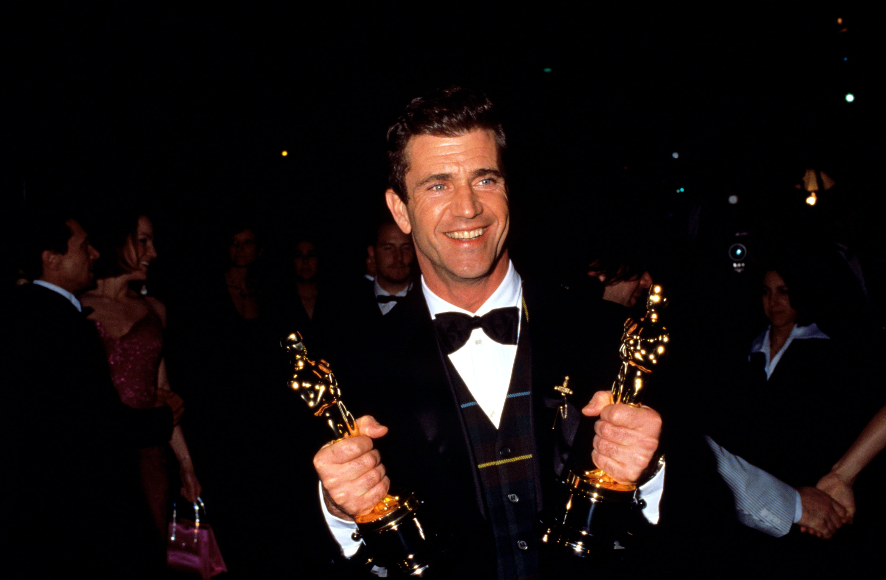 Mel Gibson holds up his Oscar trophies during the 1996 Vanity Fair Oscar Party at Morton's Restaurant in West Hollywood, California.