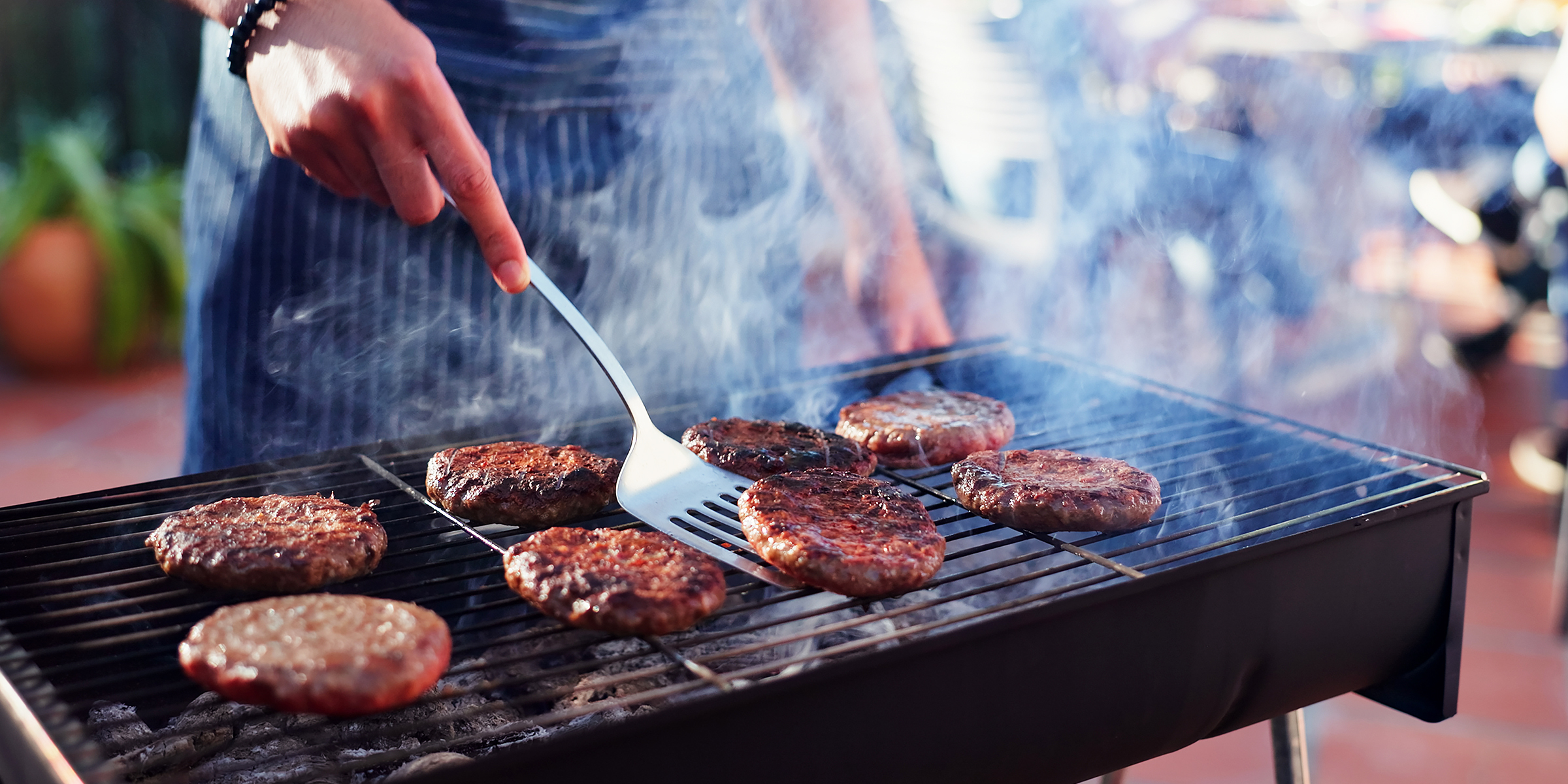 A person grilling burgers on a smoky backyard barbecue | Source: Shutterstock