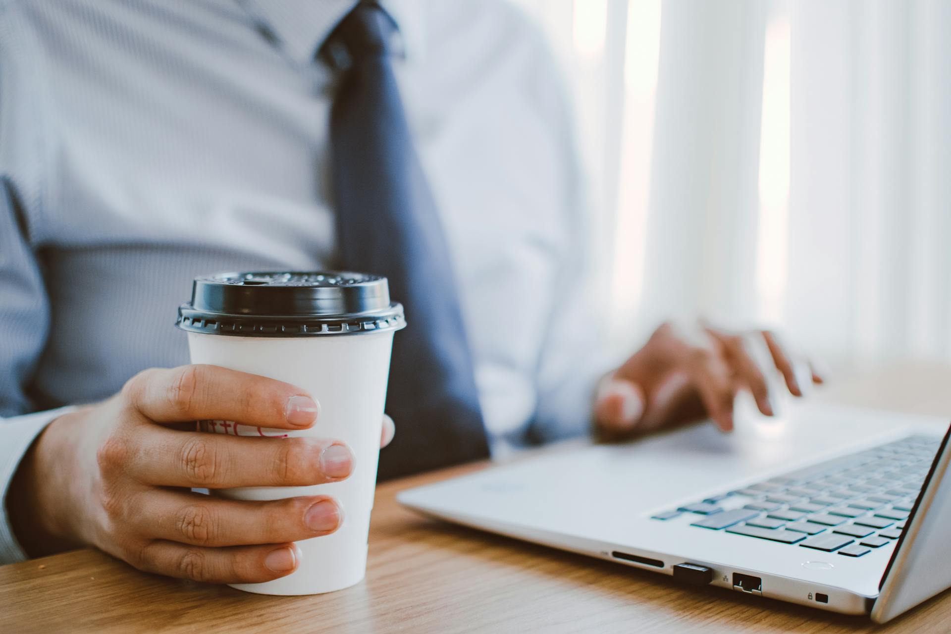 A closeup of a man working on his laptop while holding his coffee cup | Source: Pexels