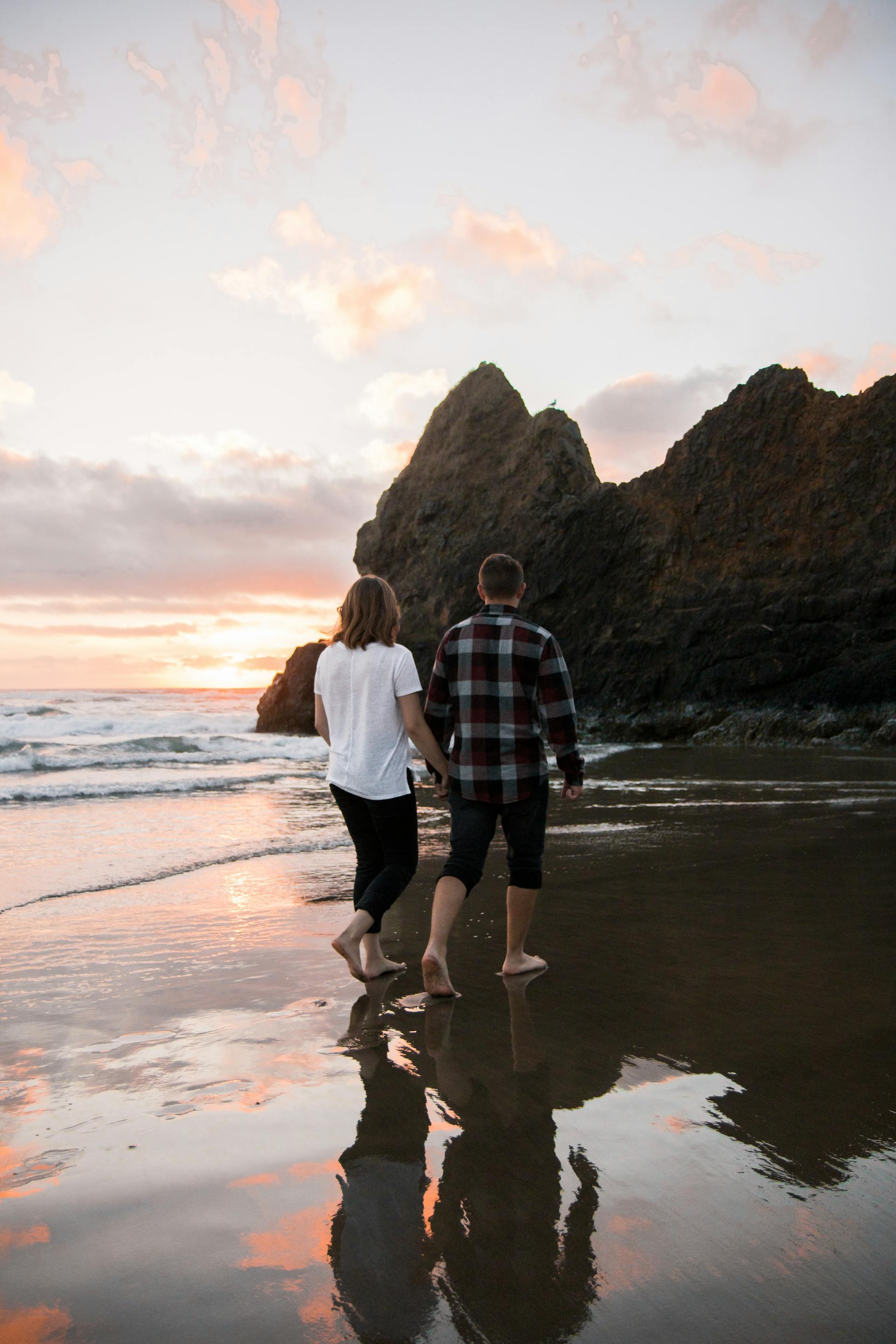 A couple holding hands while walking barefoot on the shore | Source: Pexels
