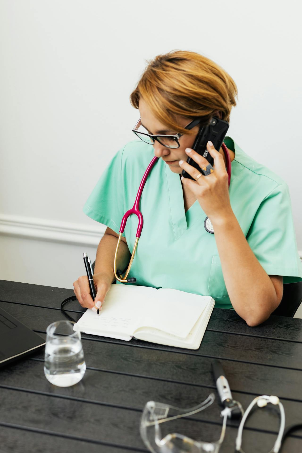 A medical staff talking on the phone while writing on a notebook | Source: Pexels