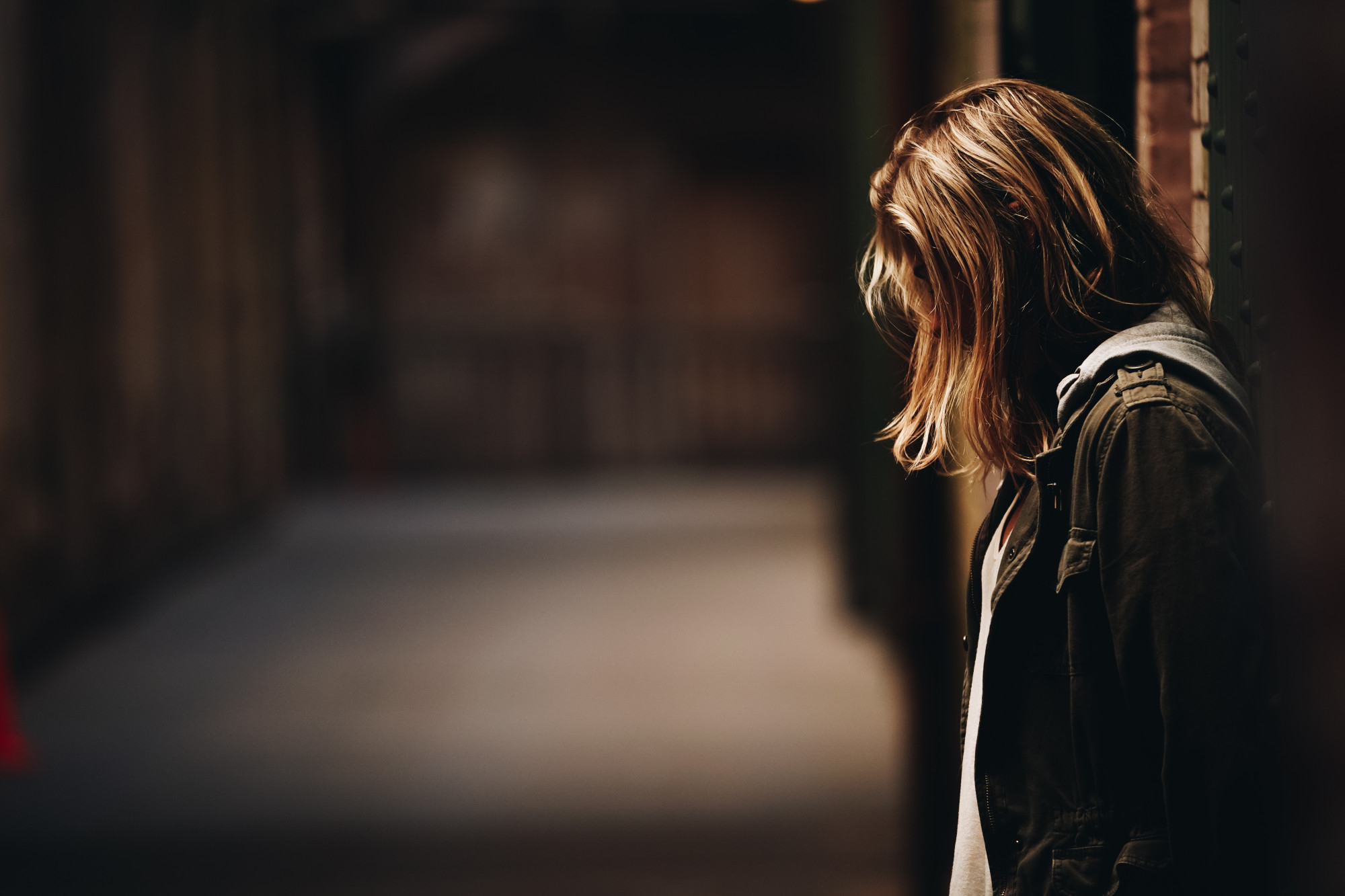 A teenage girl leaning against the wall, looking down in a hallway | Source: Freepik