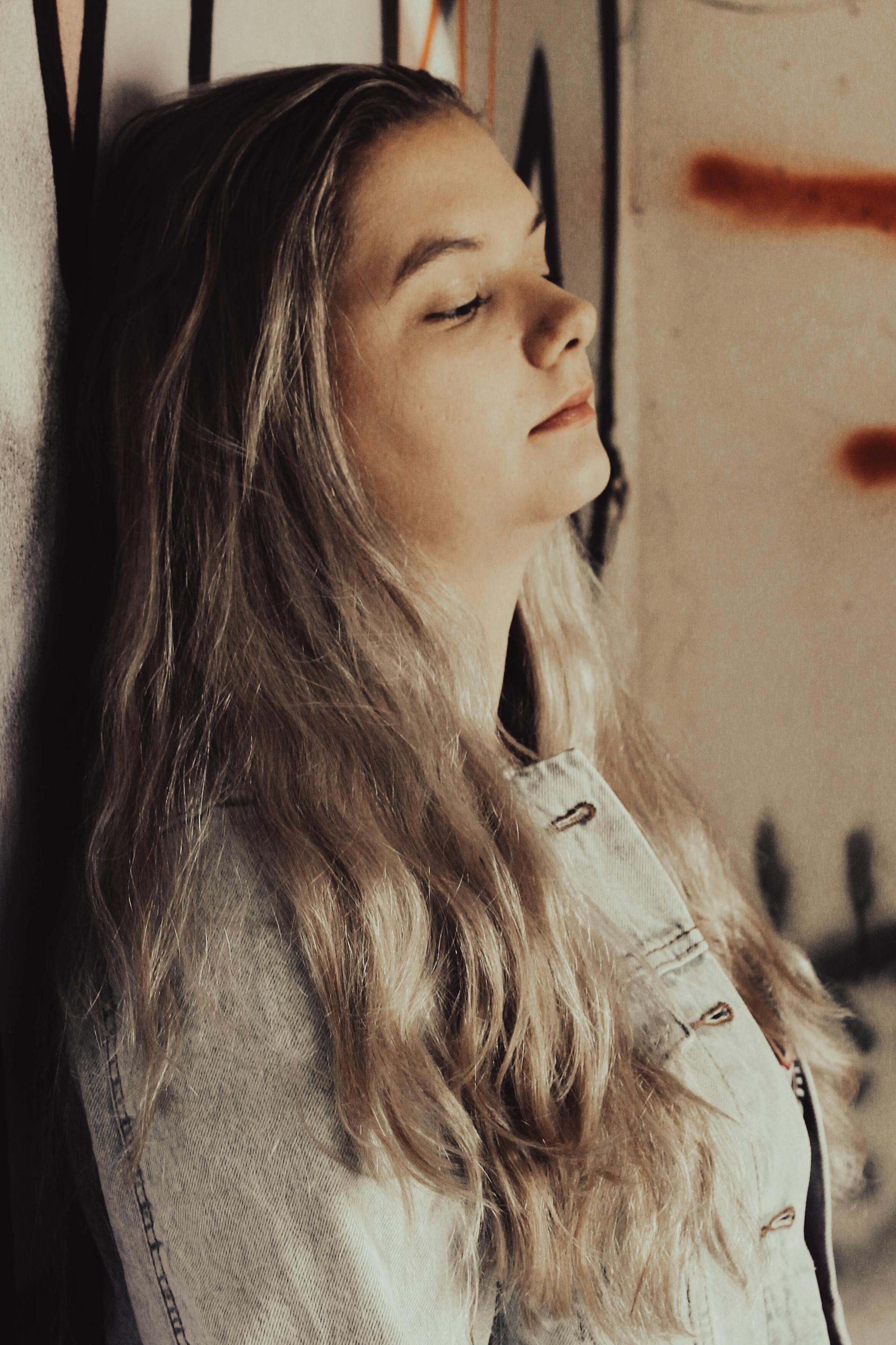 A sad woman in a denim jacket with her eyes closed, leaning against a wall | Source: Pexels