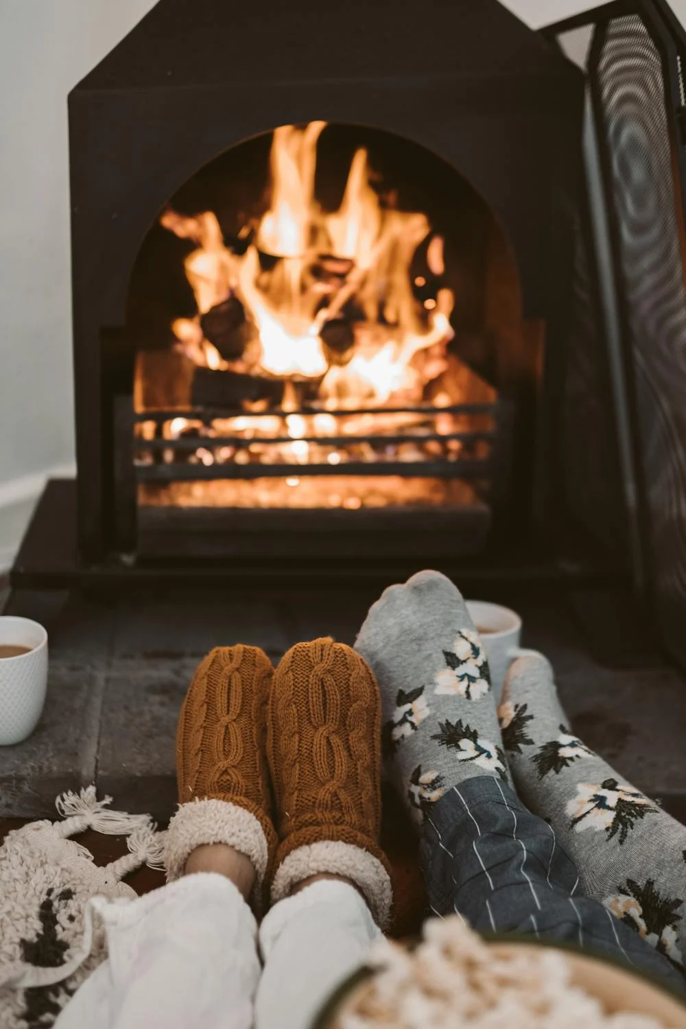 Two pairs of sock-clad feet in front of a glowing fireplace | Source: Pexels