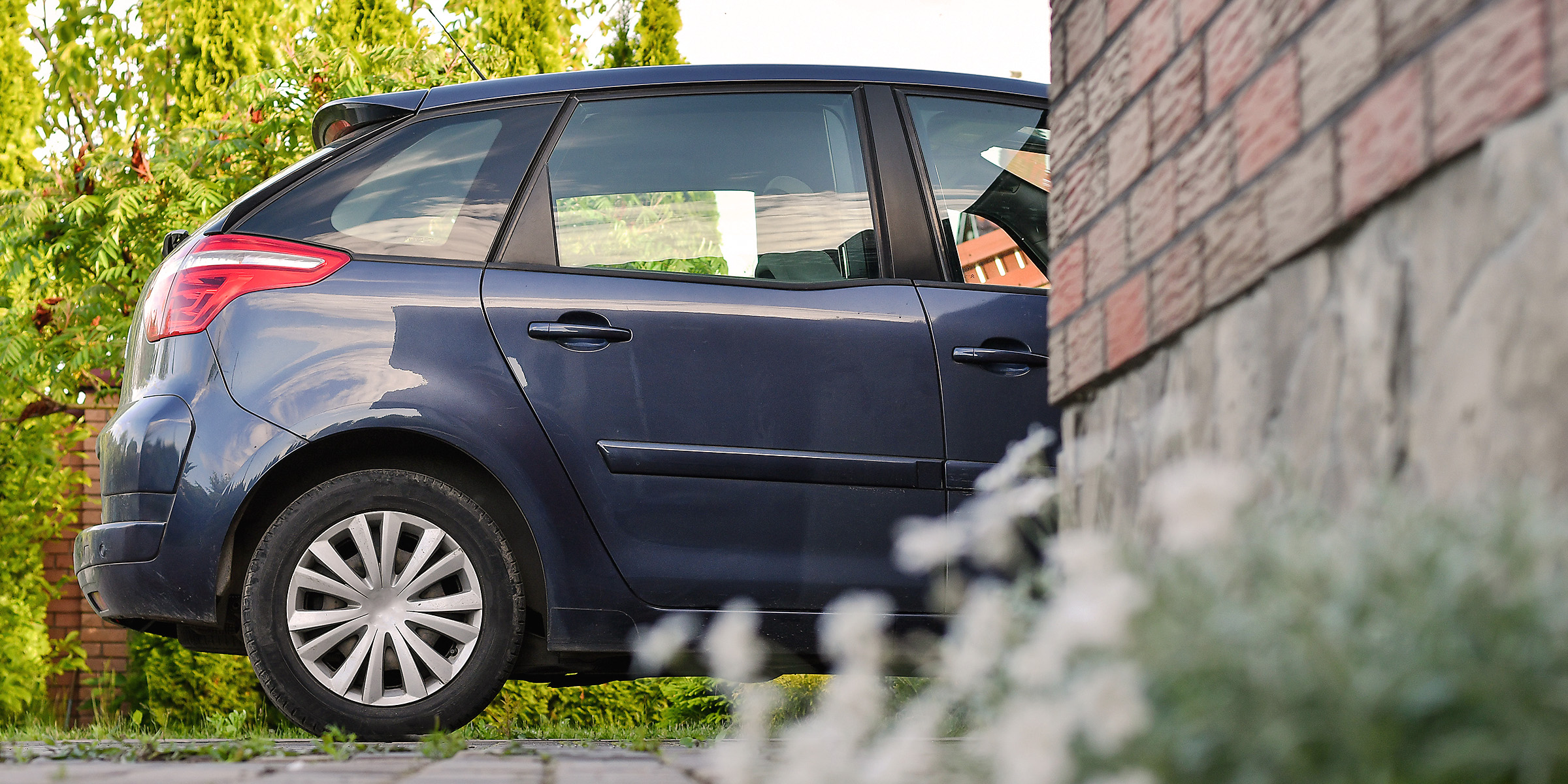 A dark blue car parked beside a brick wall in a quiet neighborhood | Source: Shutterstock