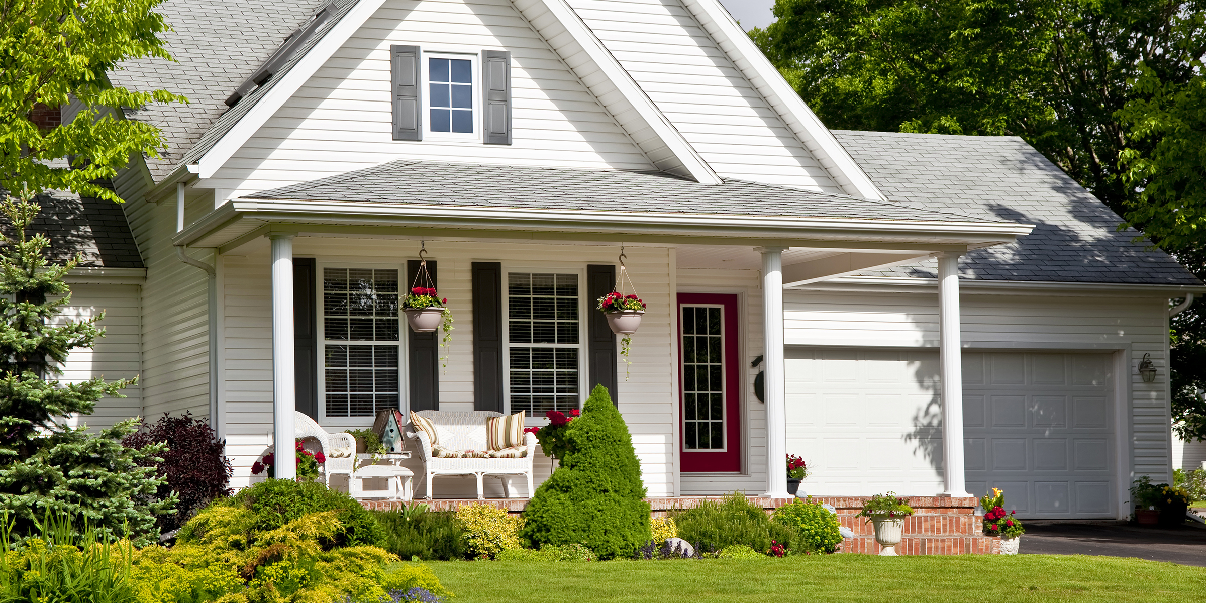 A charming suburban home with a red front door, cozy porch seating, and vibrant landscaping in full bloom | Source: Shutterstock