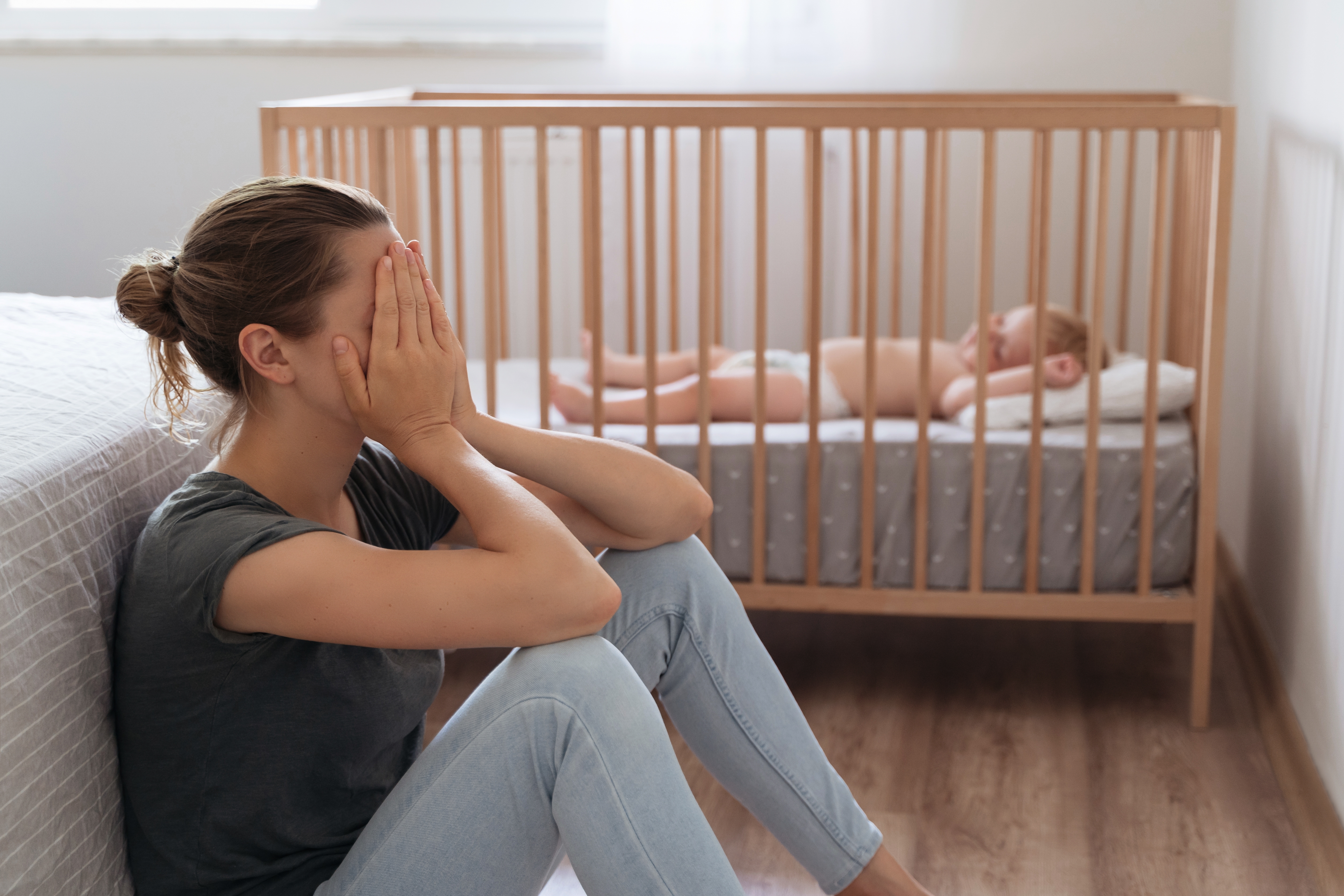 A distressed girl sitting on the floor as a baby sleeps on a crib nearby | Source" Shutterstock