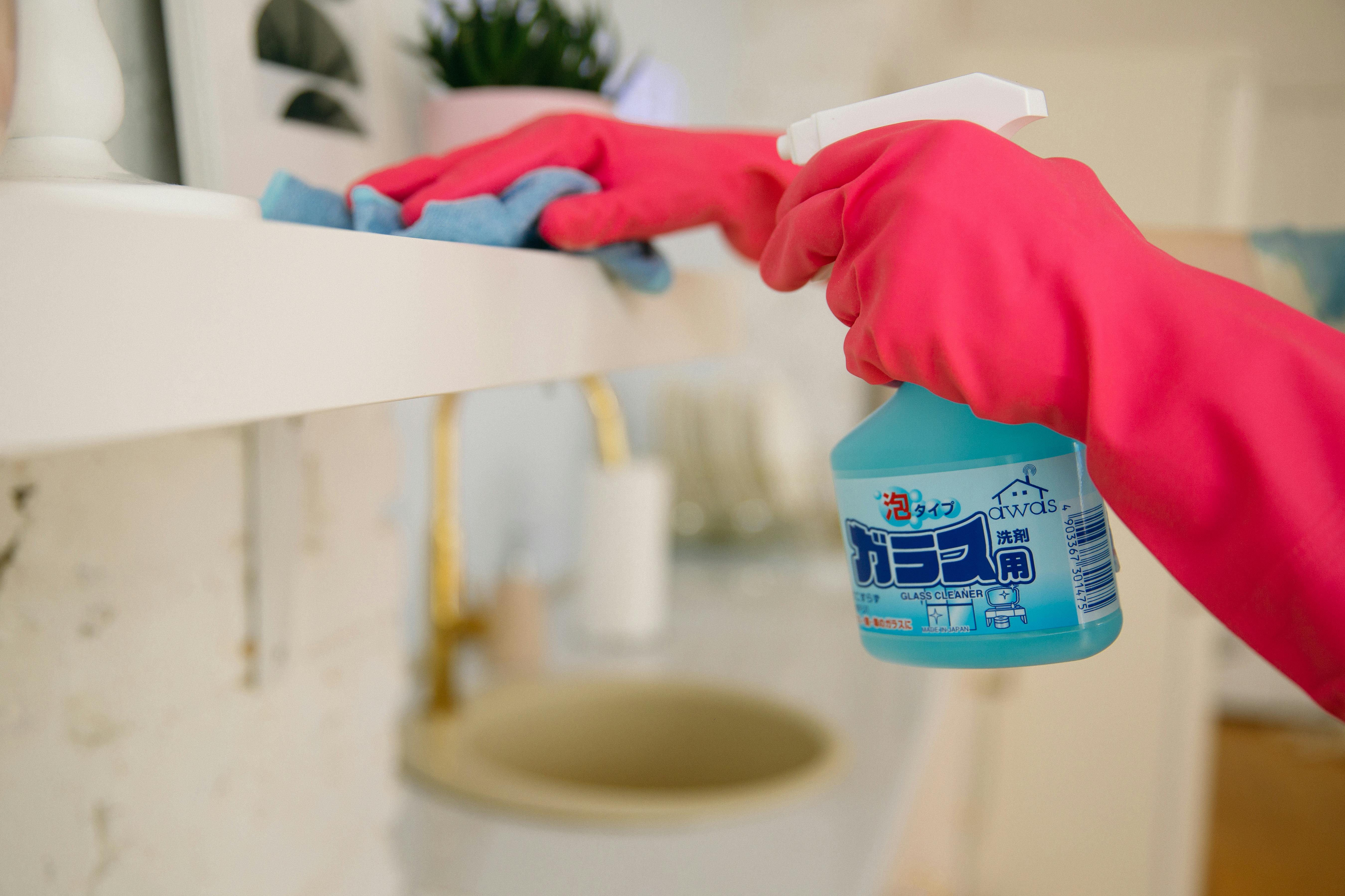 A person with gloves holding a spray bottle of glass cleaner | Source: Pexels