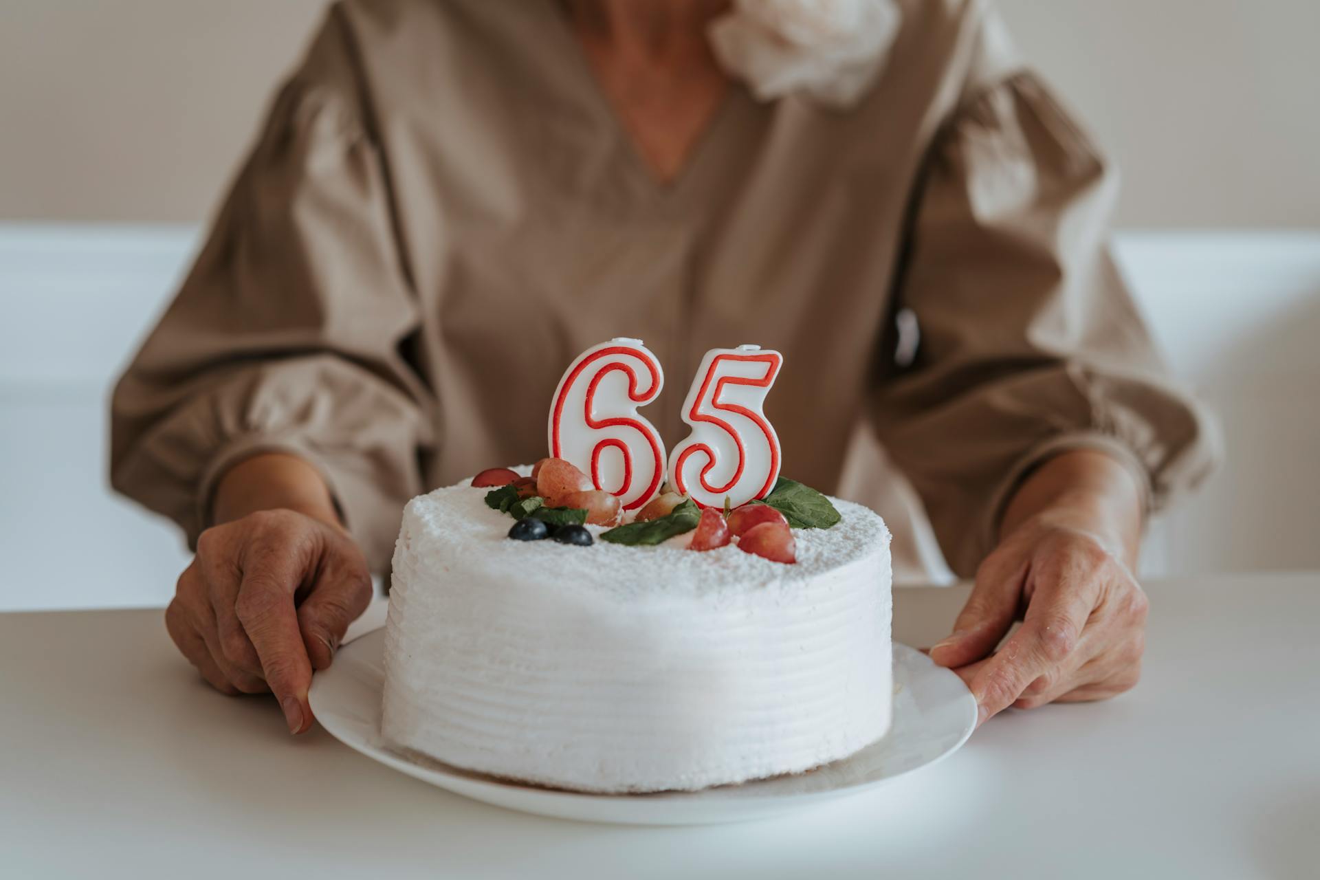 Cropped shot of an older woman holding her 65th birthday cake | Source: Pexels