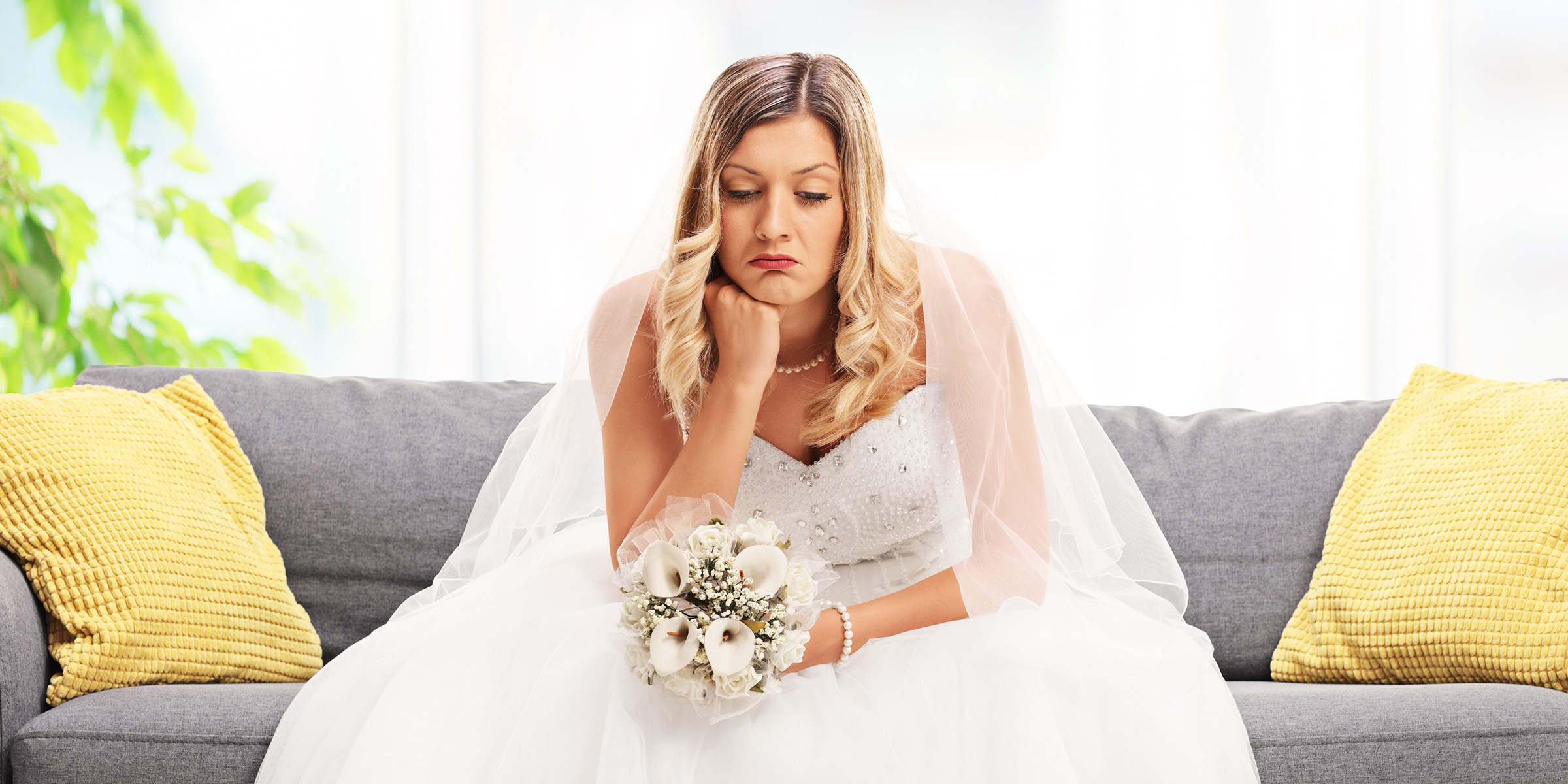 A bride sitting on a couch, looking sad and deep in thought, holding her bouquet | Source: Shutterstock