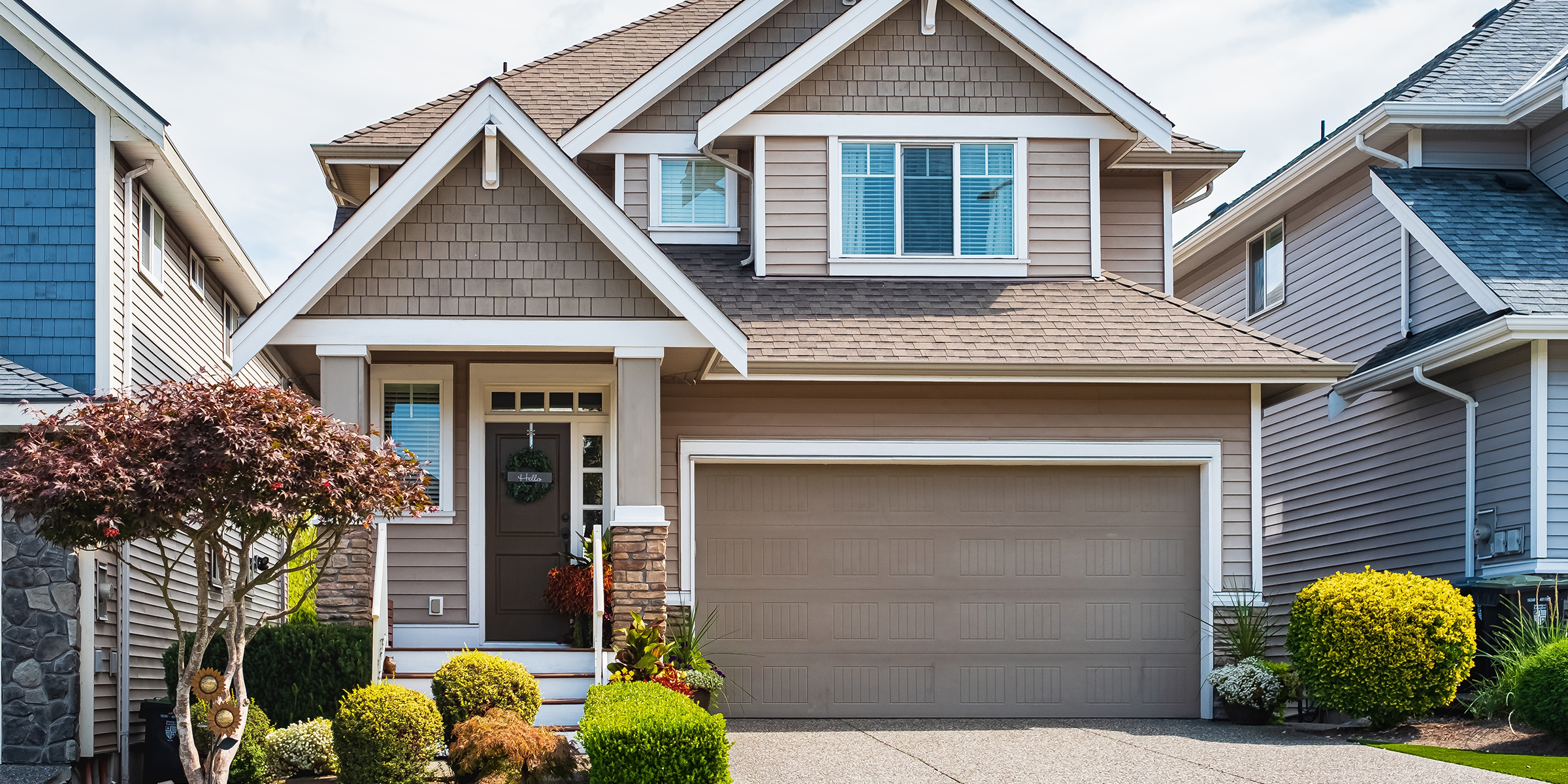 A modern suburban house with a neatly trimmed yard, beige siding, and a garage | Source: Shutterstock