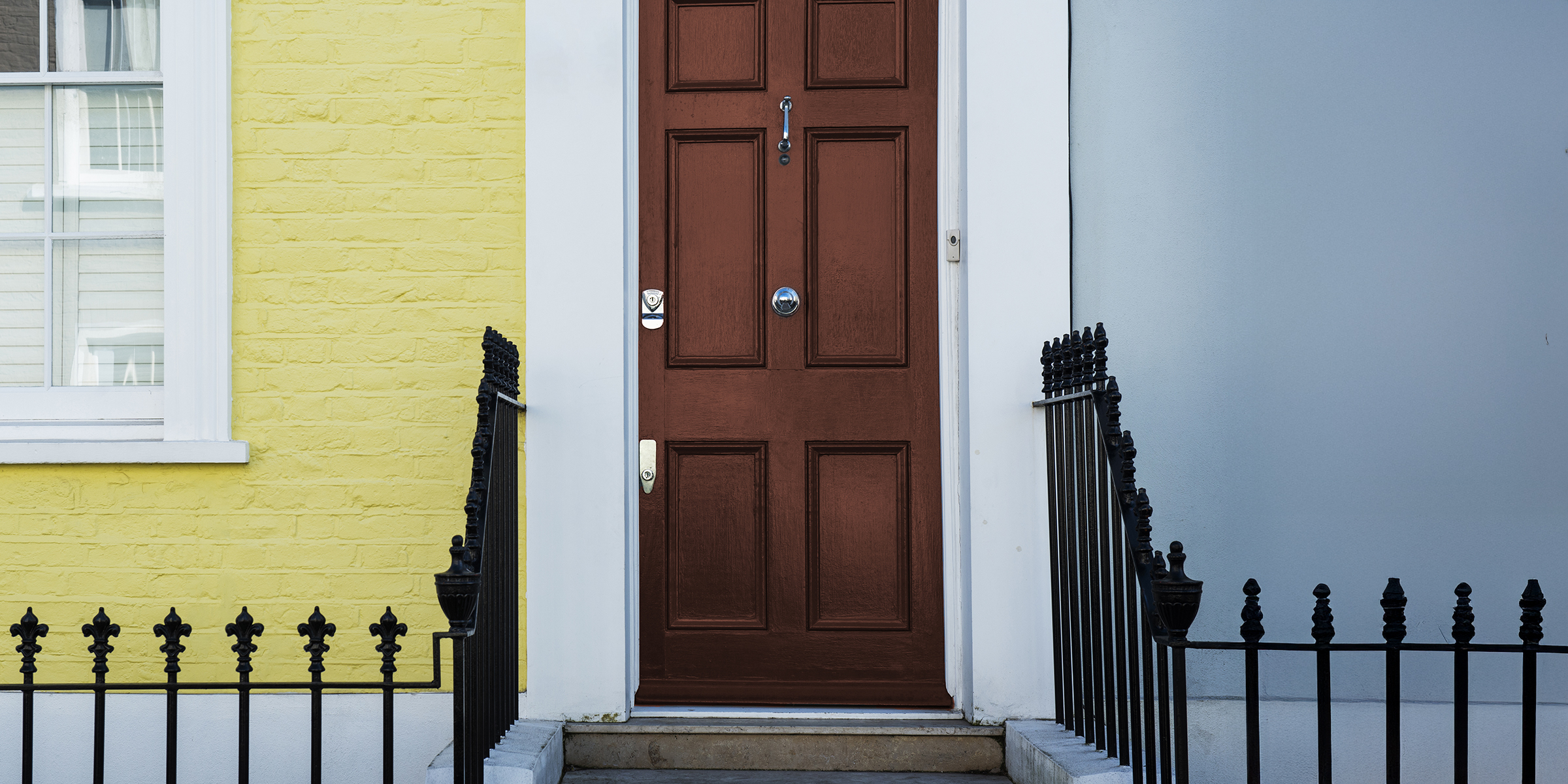 A brown front door framed by a yellow brick wall and soft blue siding | Source: Freepik