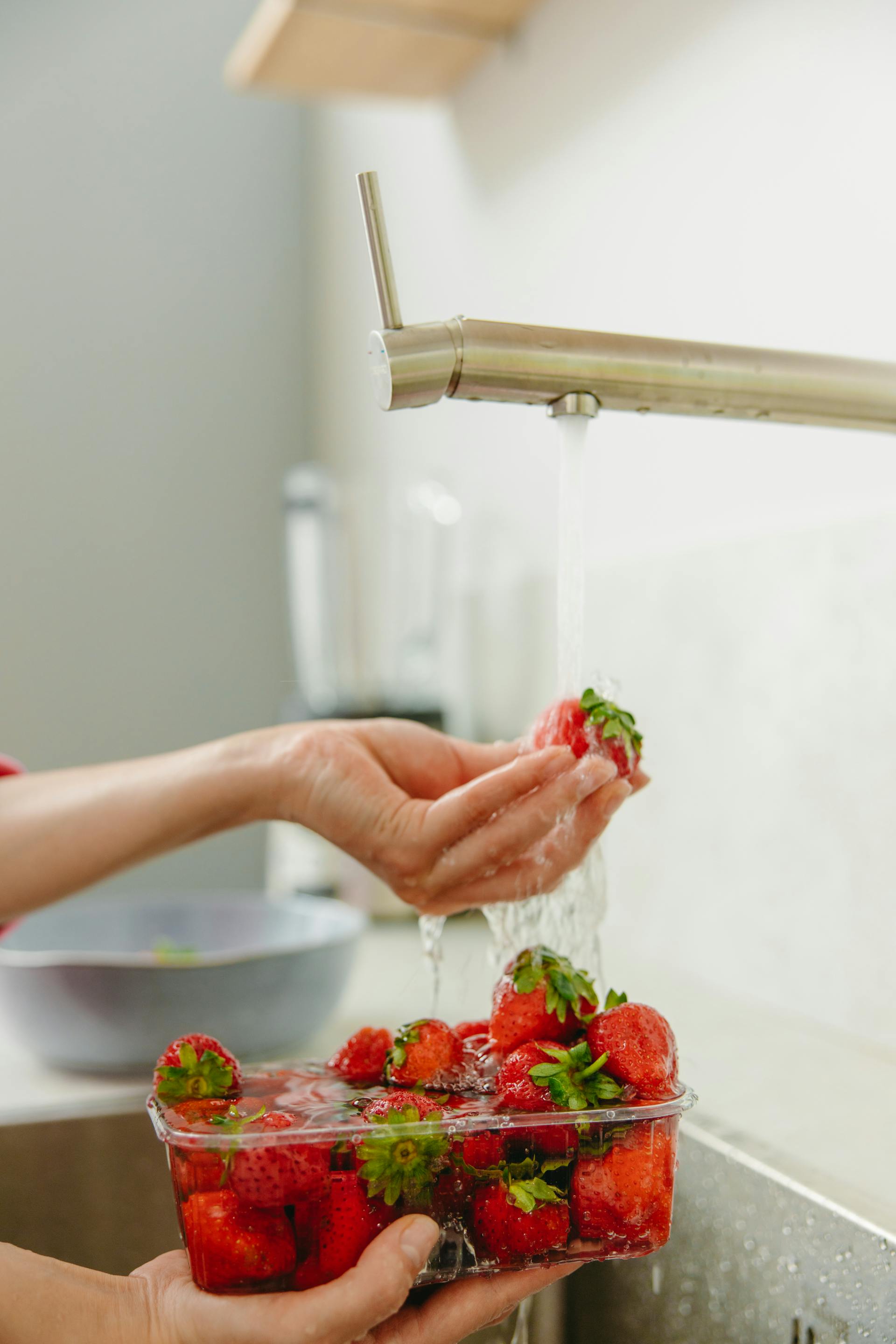 A close-up shot of a woman washing strawberries with running water in the kitchen | Source: Pexels