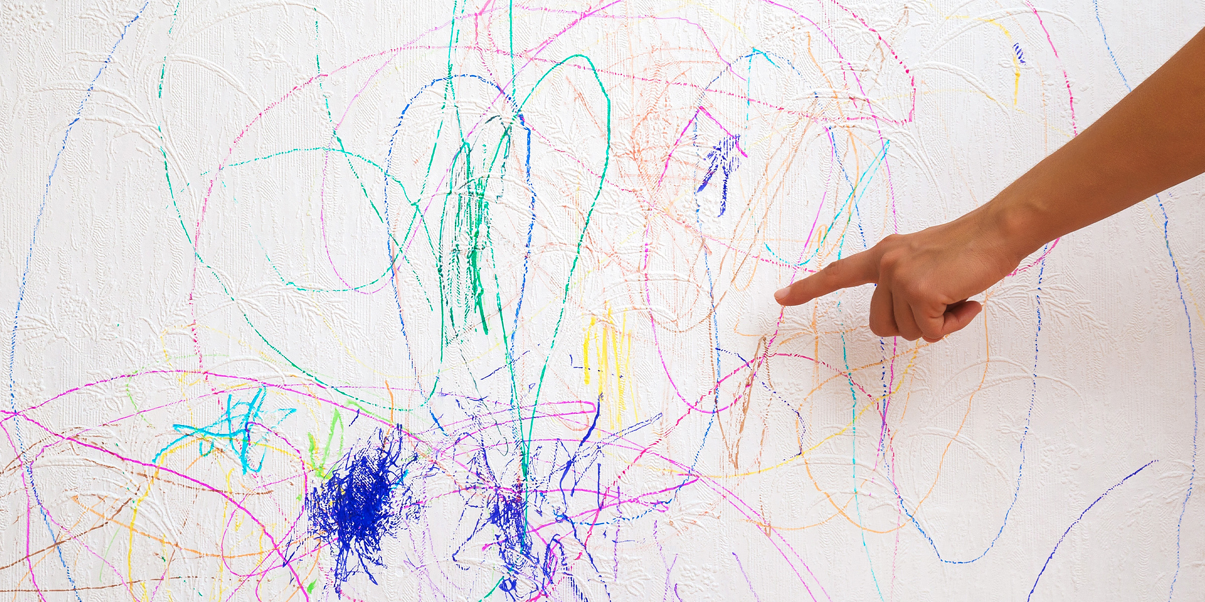 A finger pointing to colorful scratches on a wall | Source: Shutterstock