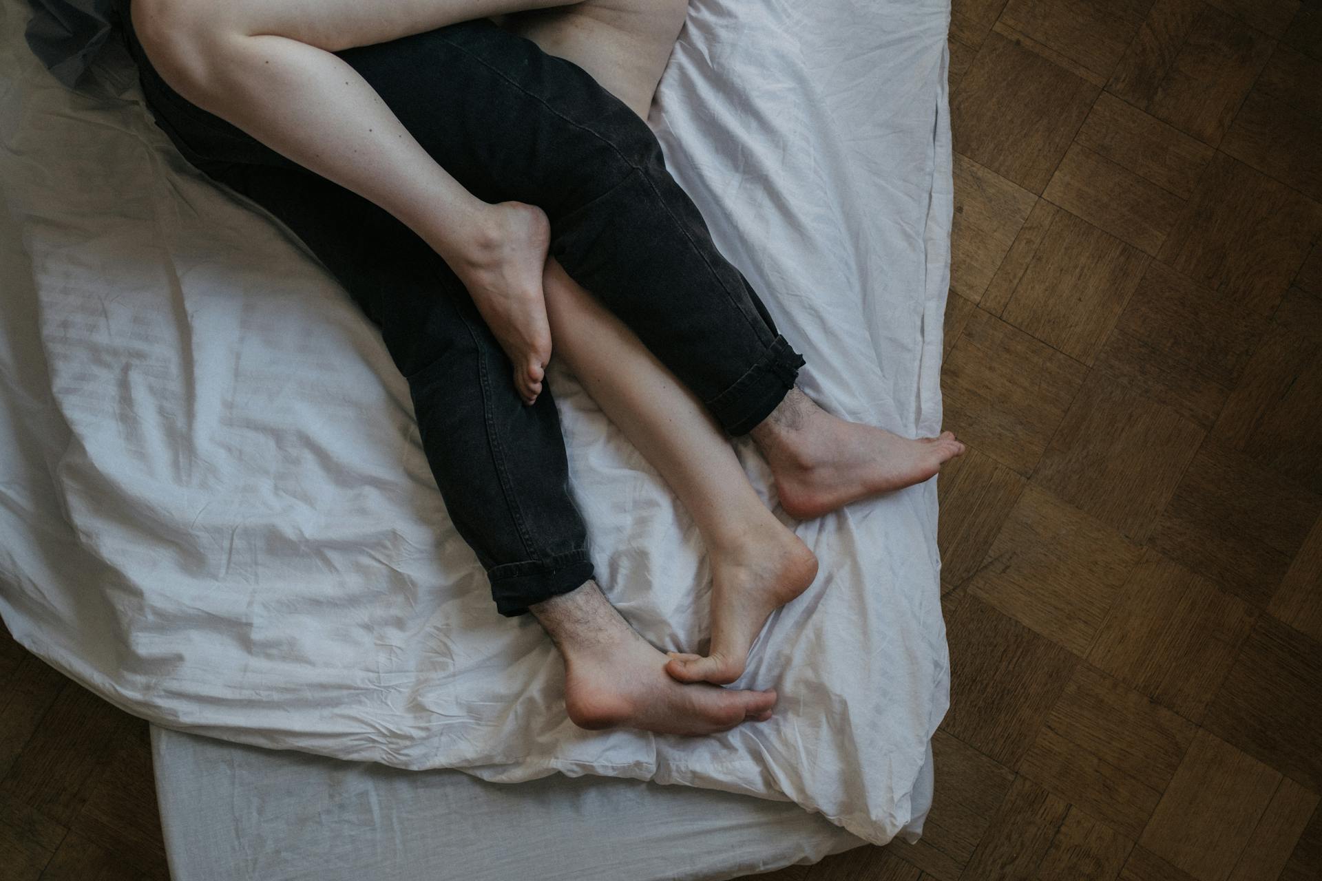 Two people lying on a bed with their legs intertwined | Source: Pexels