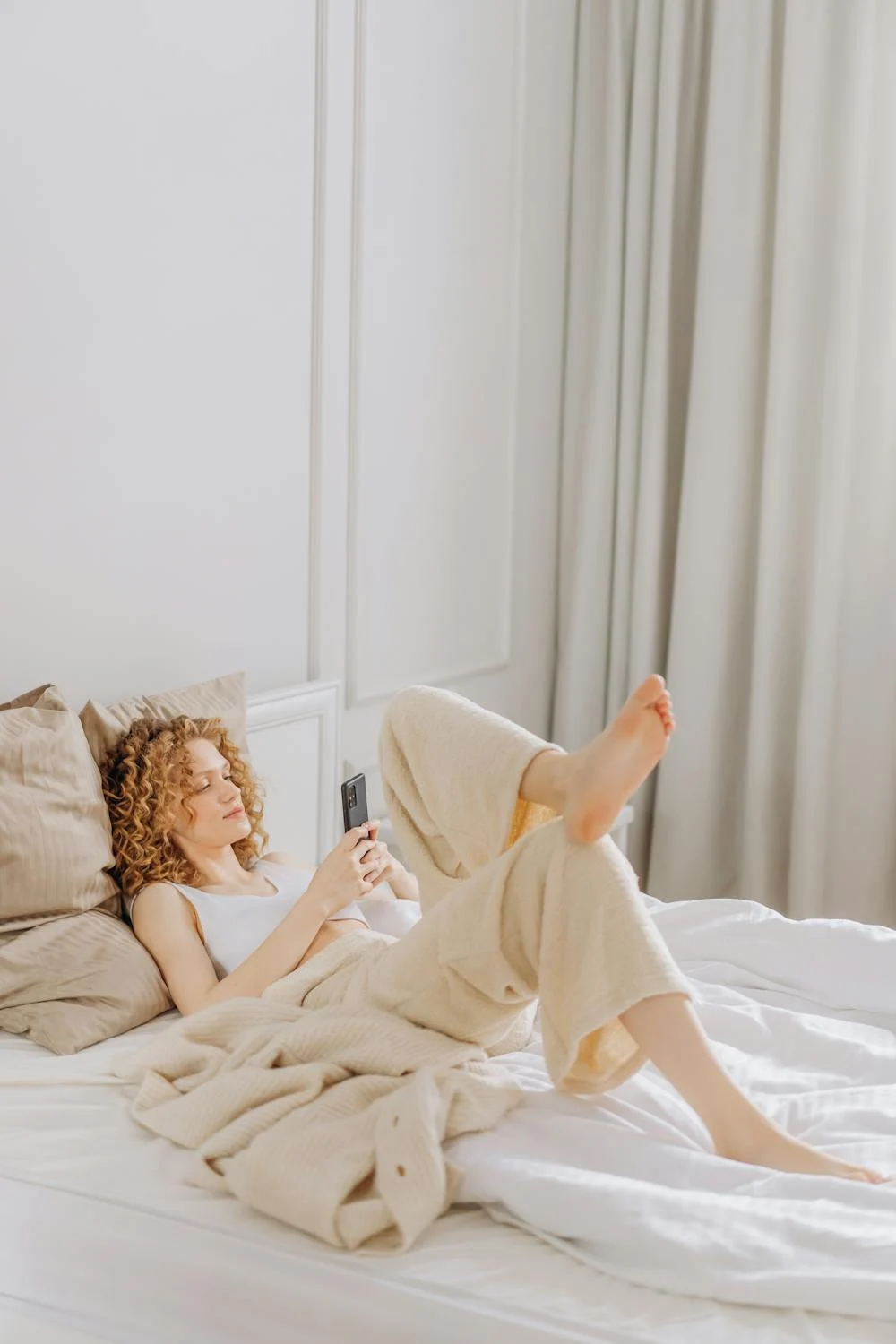 Une femme heureuse sur son téléphone dans son lit ⏐ Source : Pexels