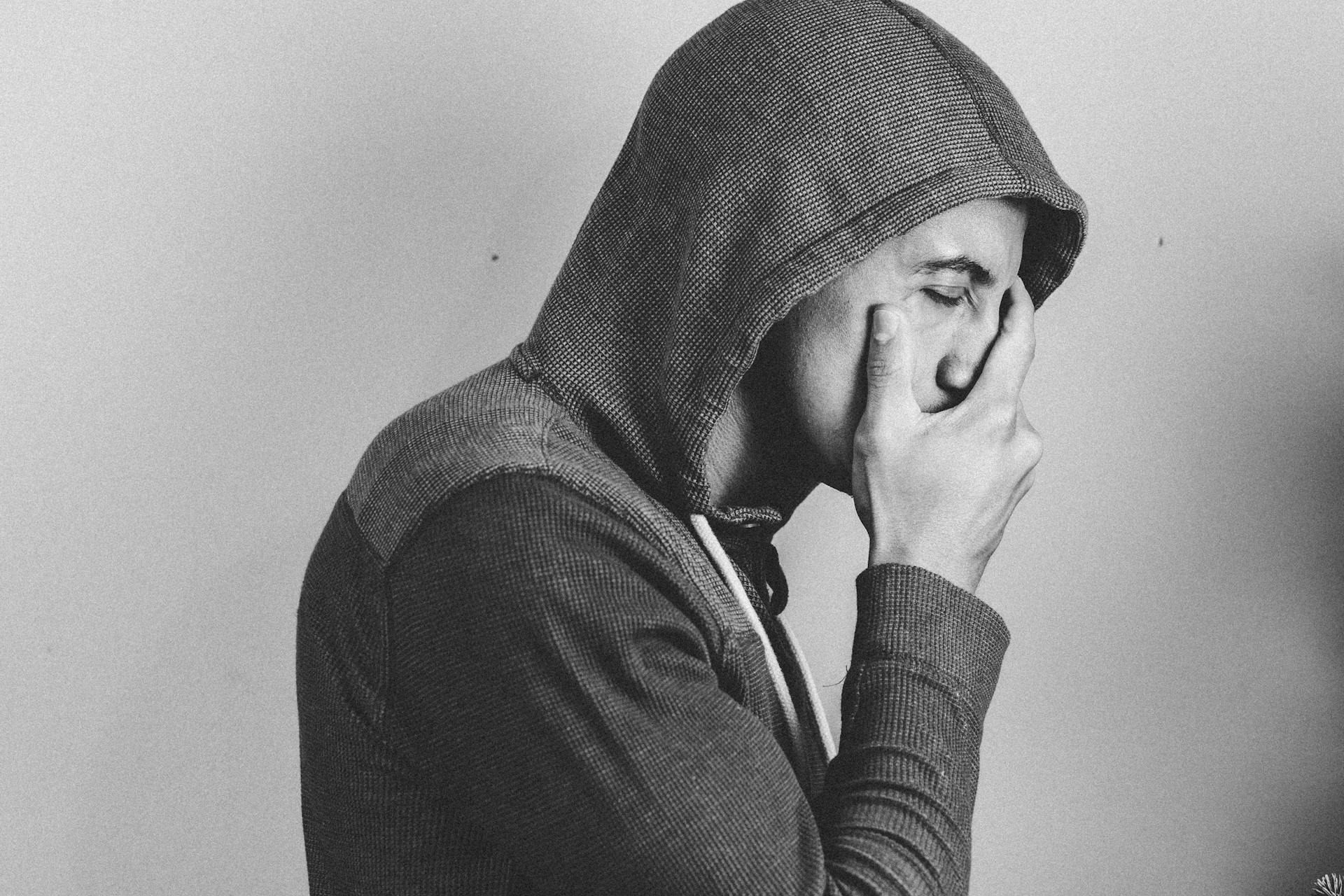 A man in a hoodie holding his face | Source: Pexels