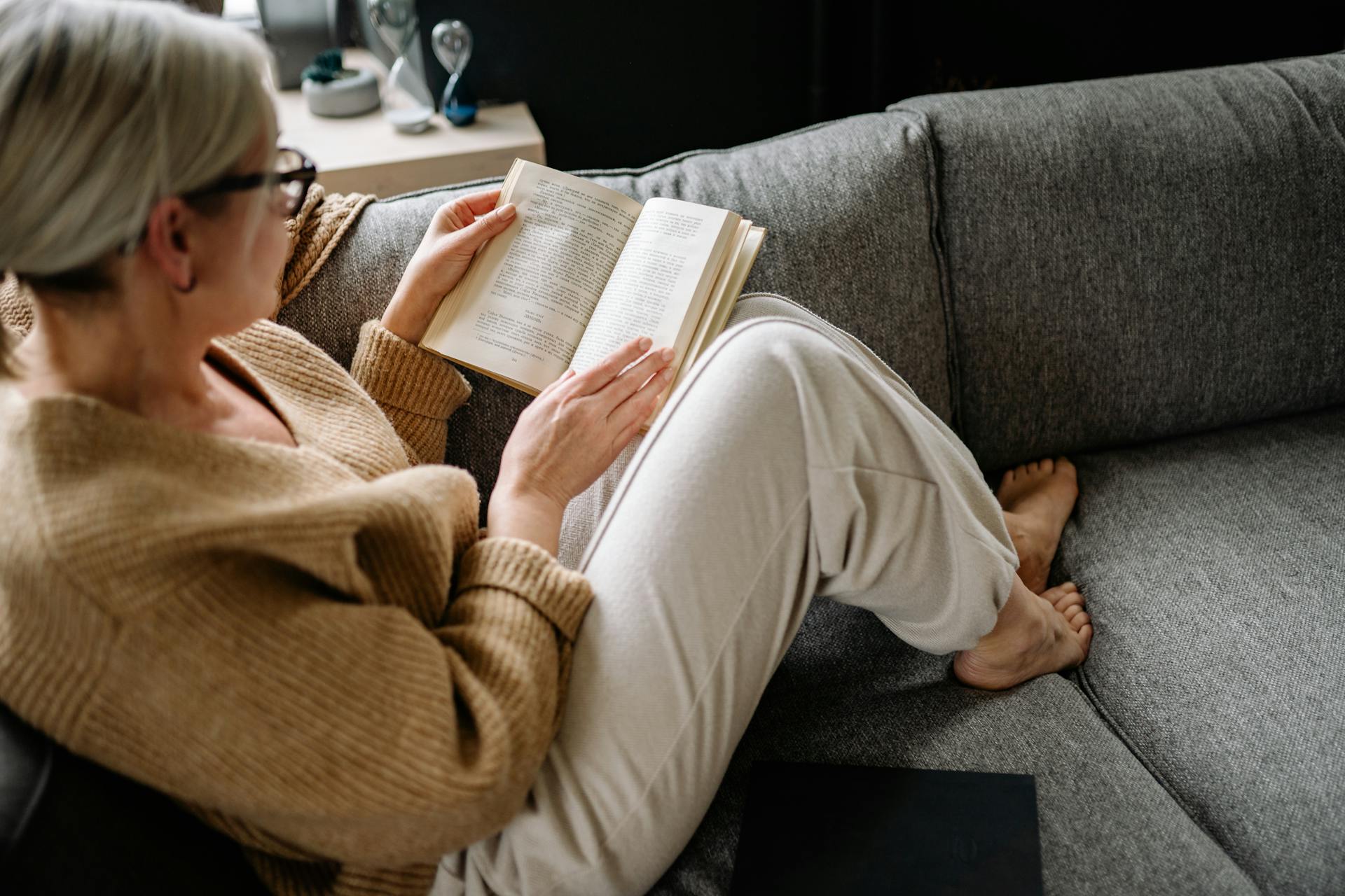 A senior woman reading a book while sitting on a sofa | Source: Pexels