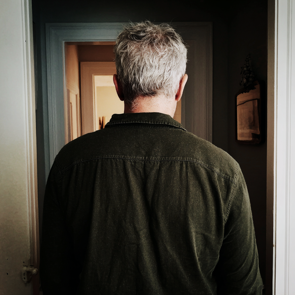 The rear view of an older man standing in a home hallway | Source: Midjourney