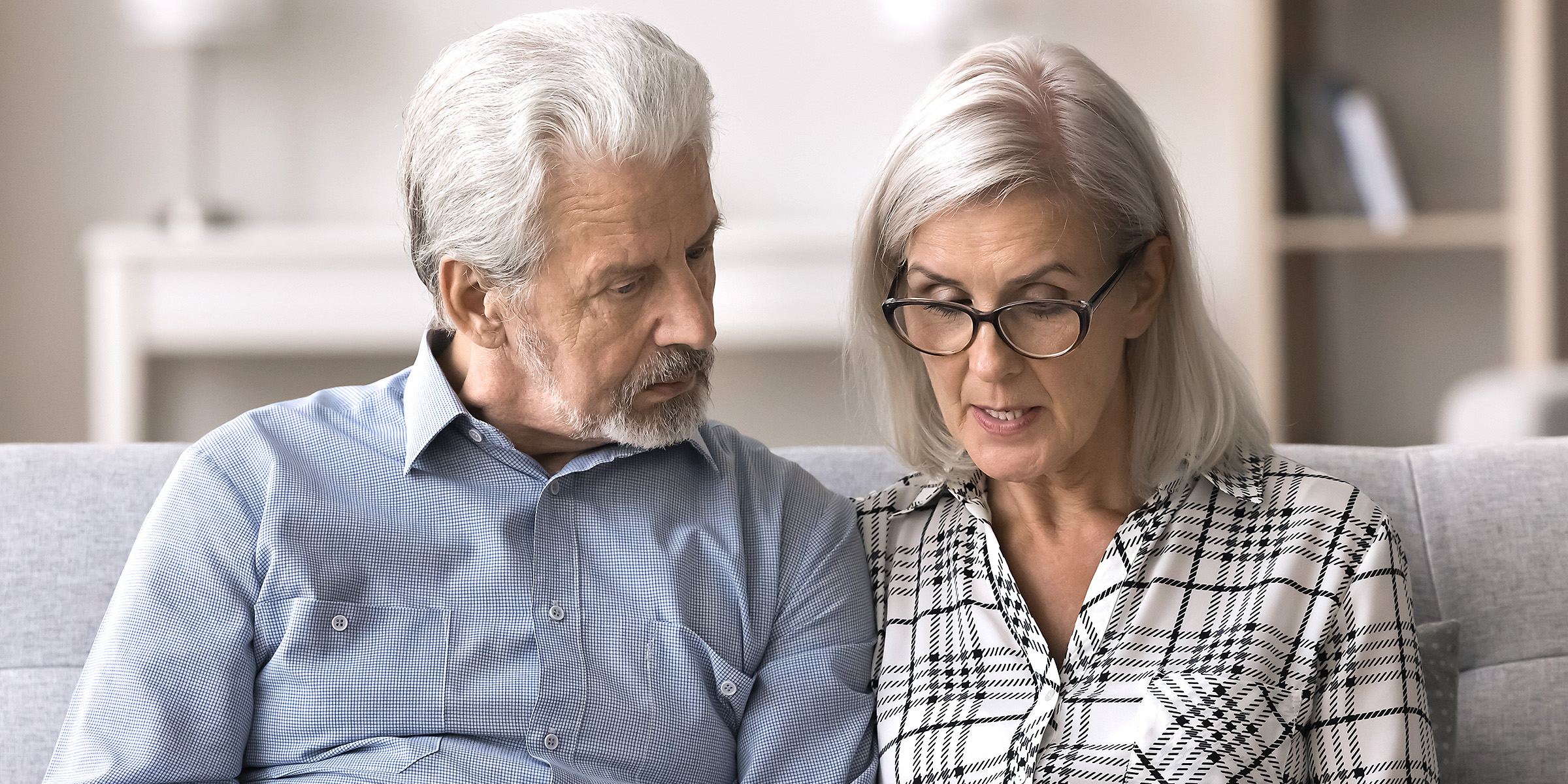 An older couple sitting closely on a couch, looking serious | Source: Shutterstock