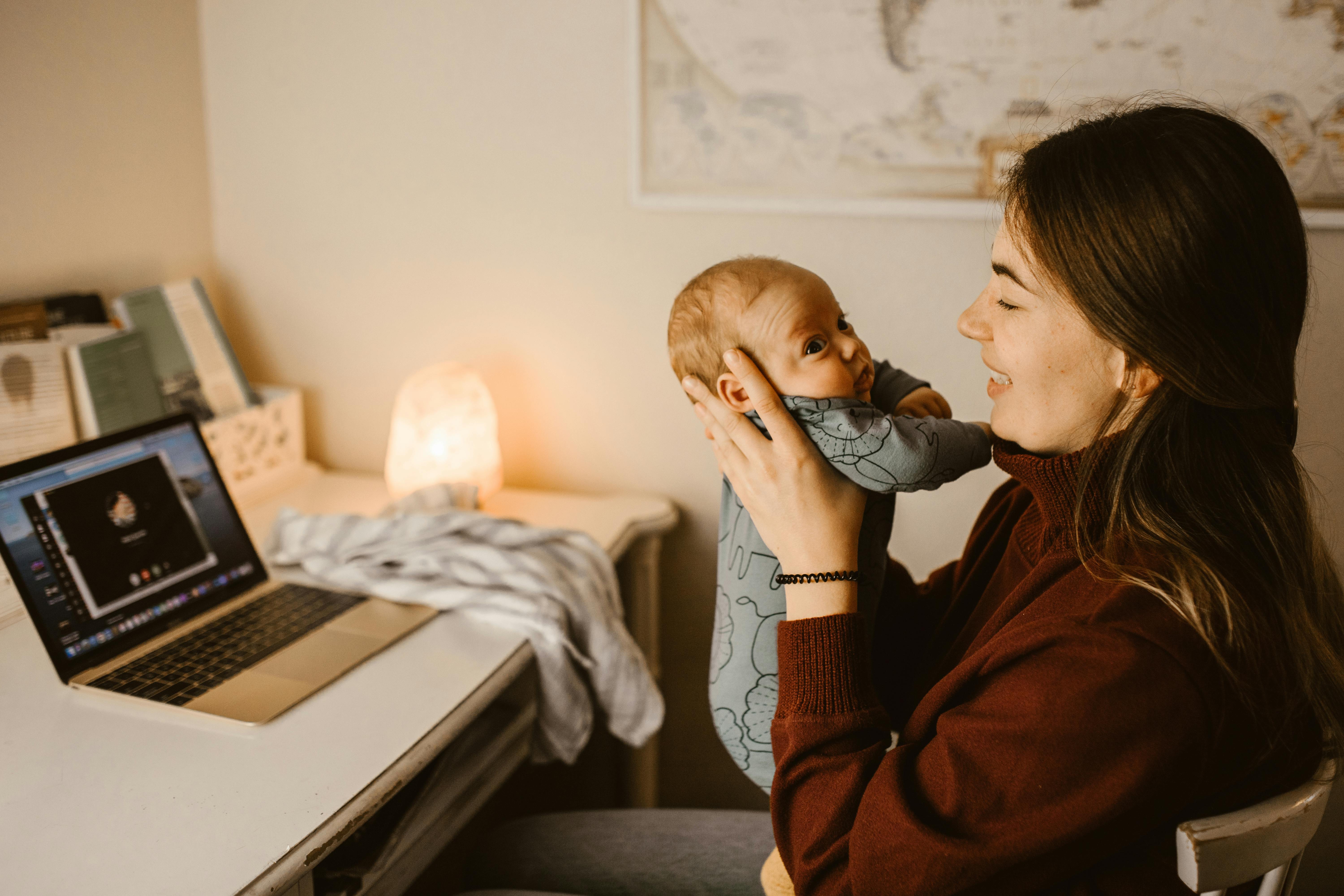 A woman holding her baby while seated at her desk | Source: Pexels