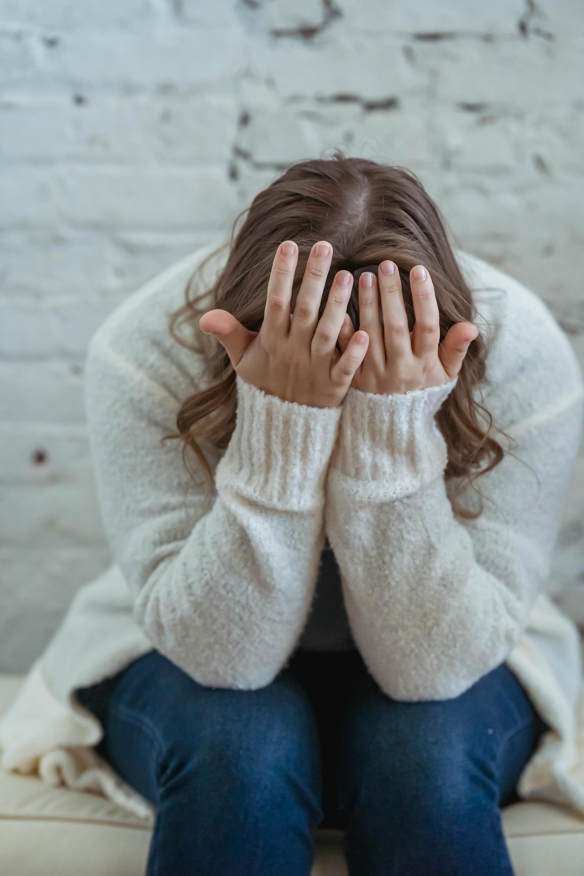 A distressed woman covering her face with her hands while sitting at home | Source: Pexels