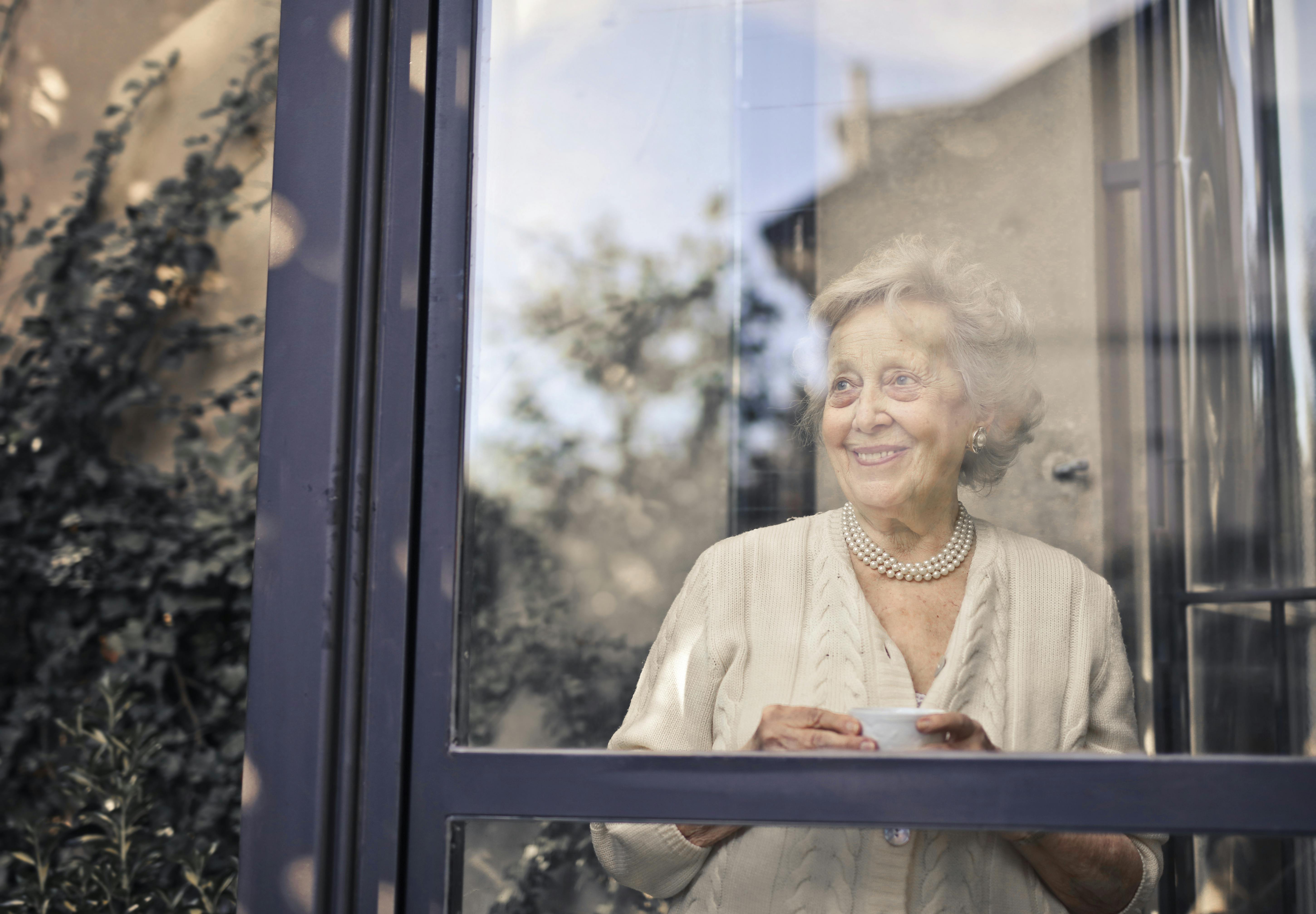 A smiling elderly woman looking out of her window | Source: Pexels