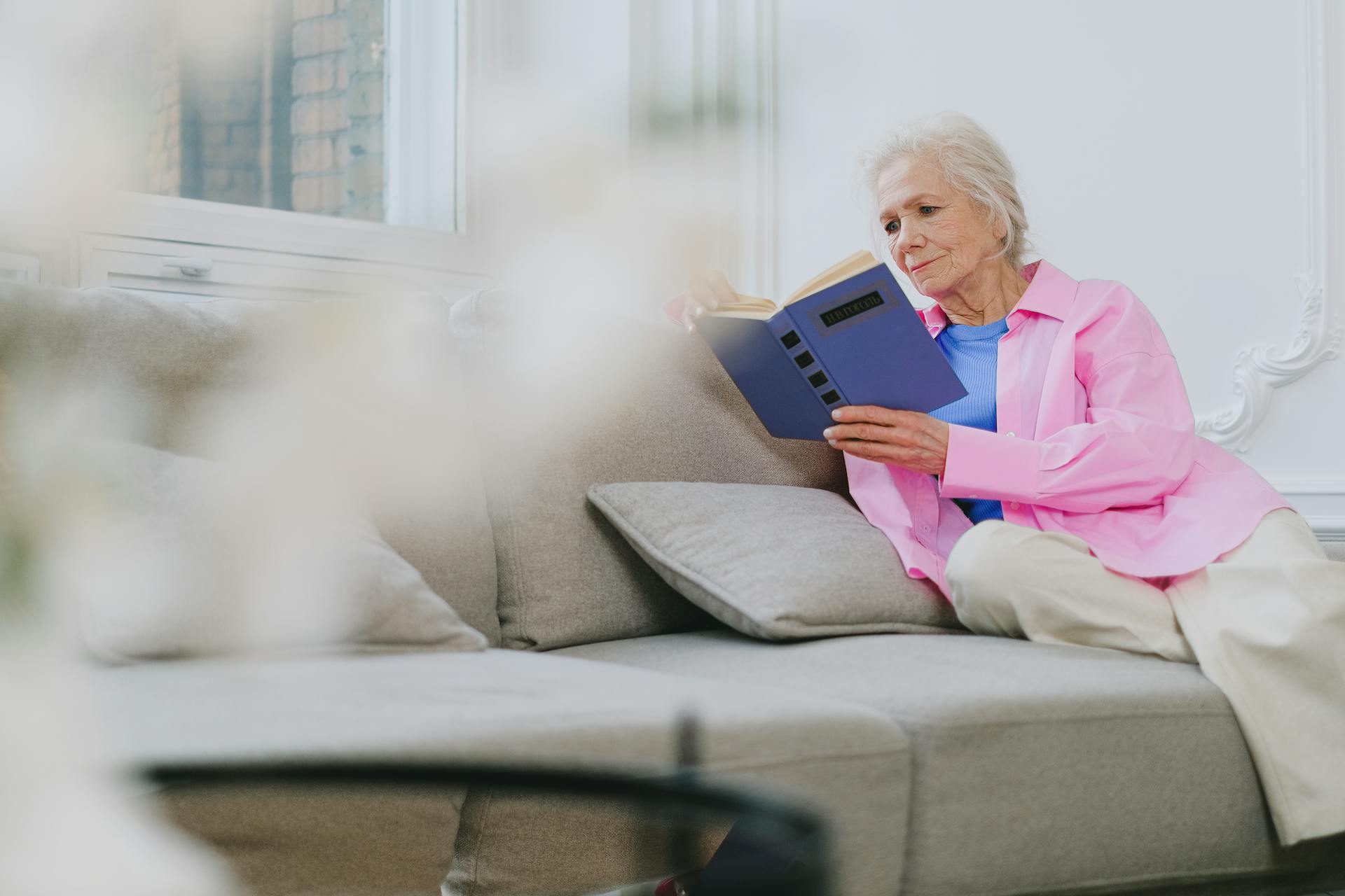 An elderly woman sitting on the couch and reading a book | Source: Pexels