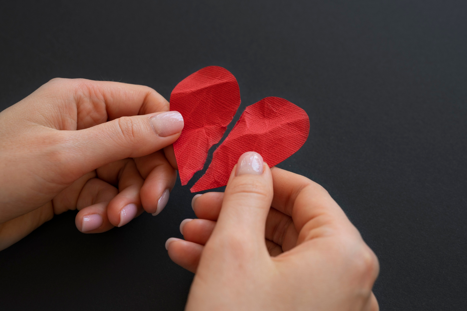 A woman holding a broken paper heart | Source: Freepik