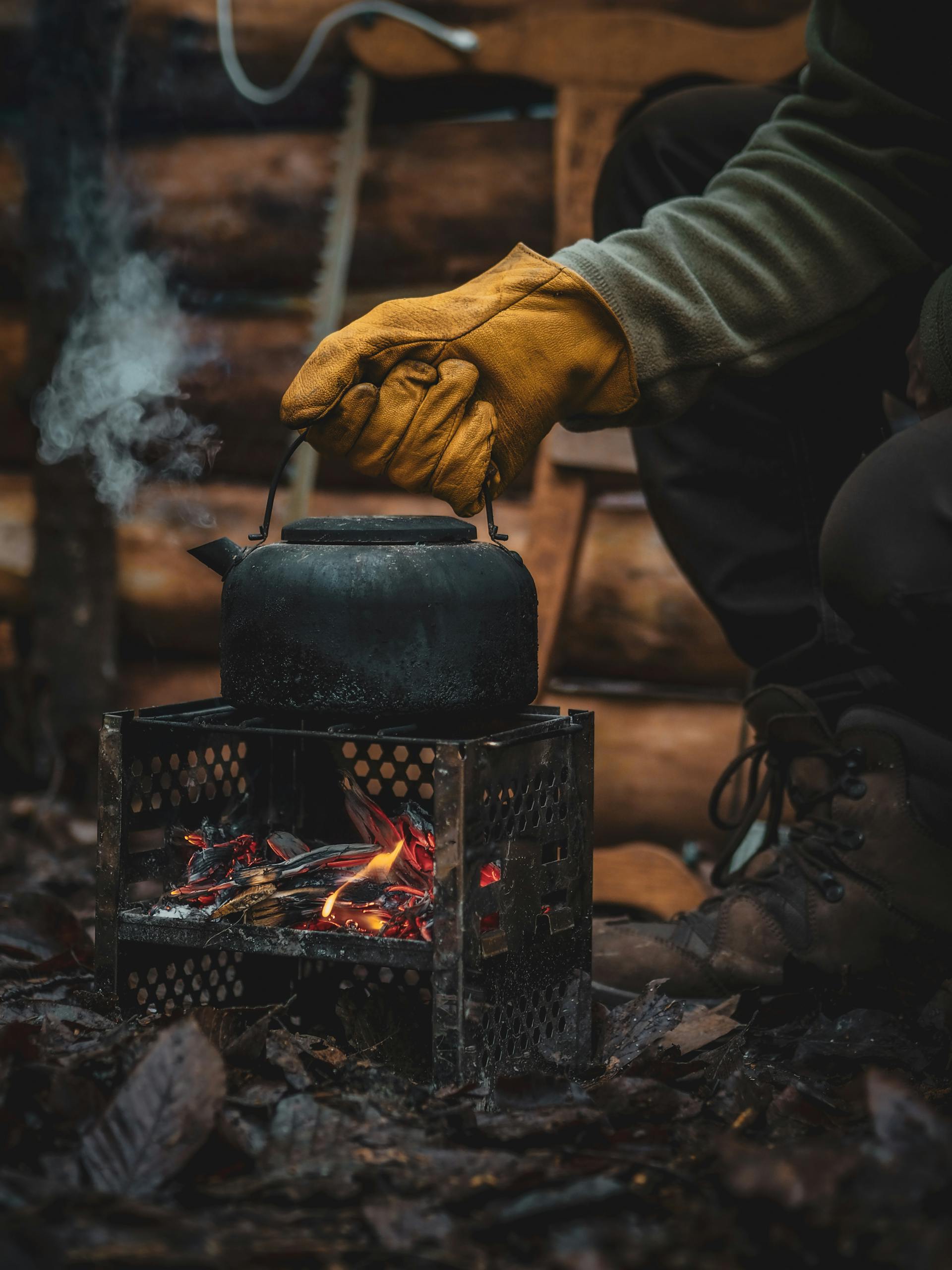 A close-up shot of a person wearing a hand glove and holding a kettle over fire | Source: Pexels