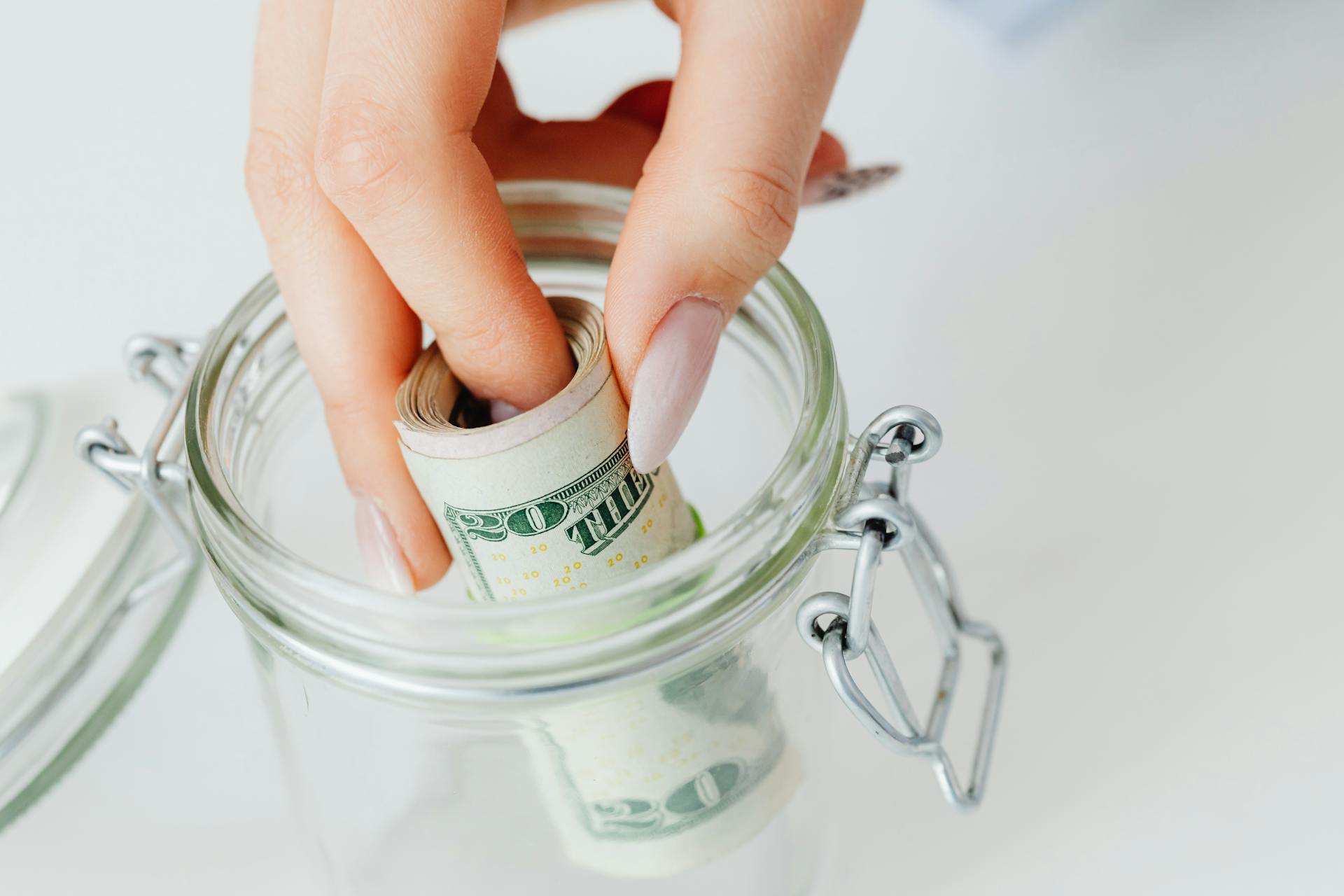 A woman taking a roll of dollar bills from a glass jar | Source: Pexels