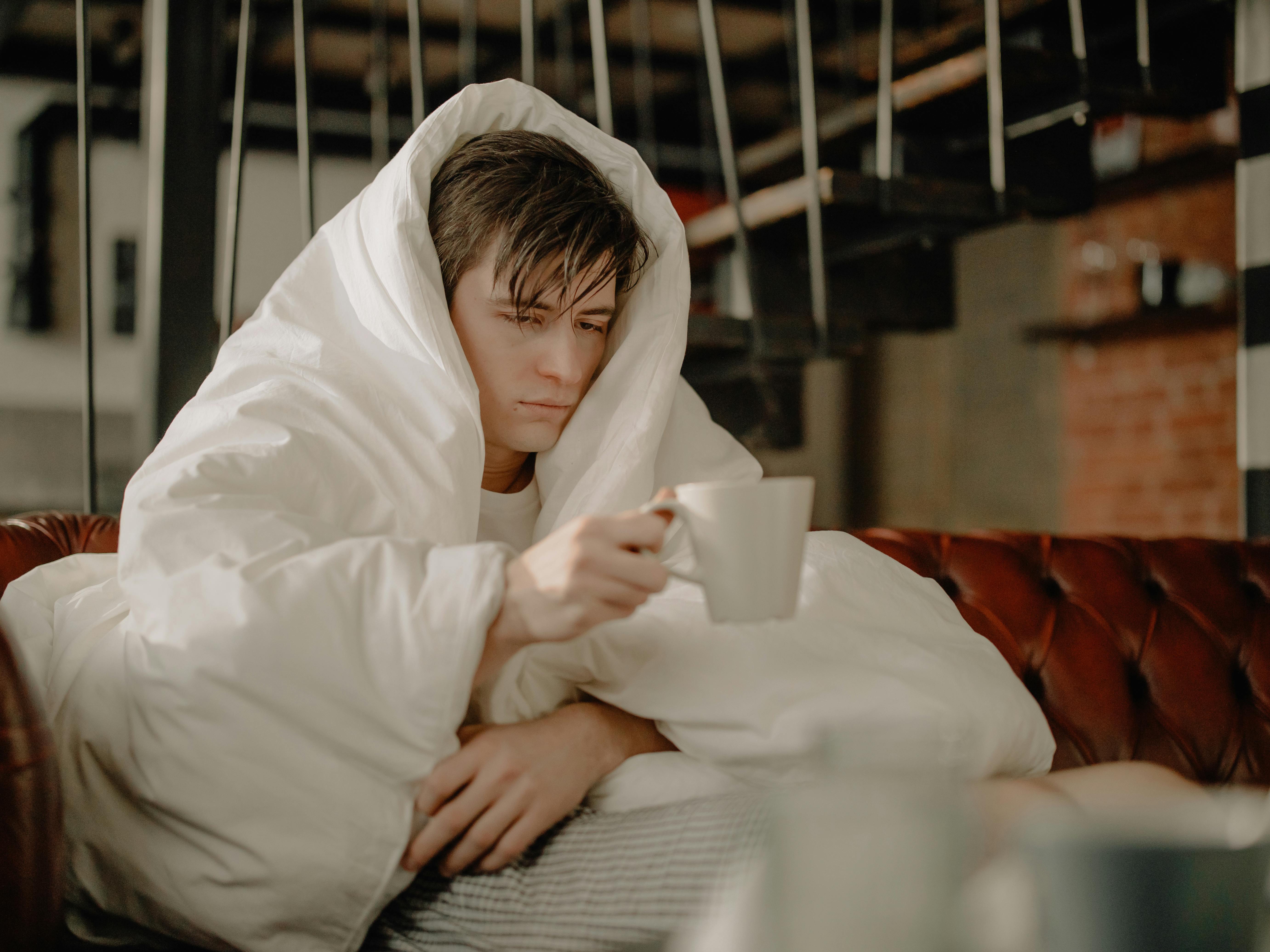 A miserable man covered in bedding while sitting on a couch | Source: Pexels