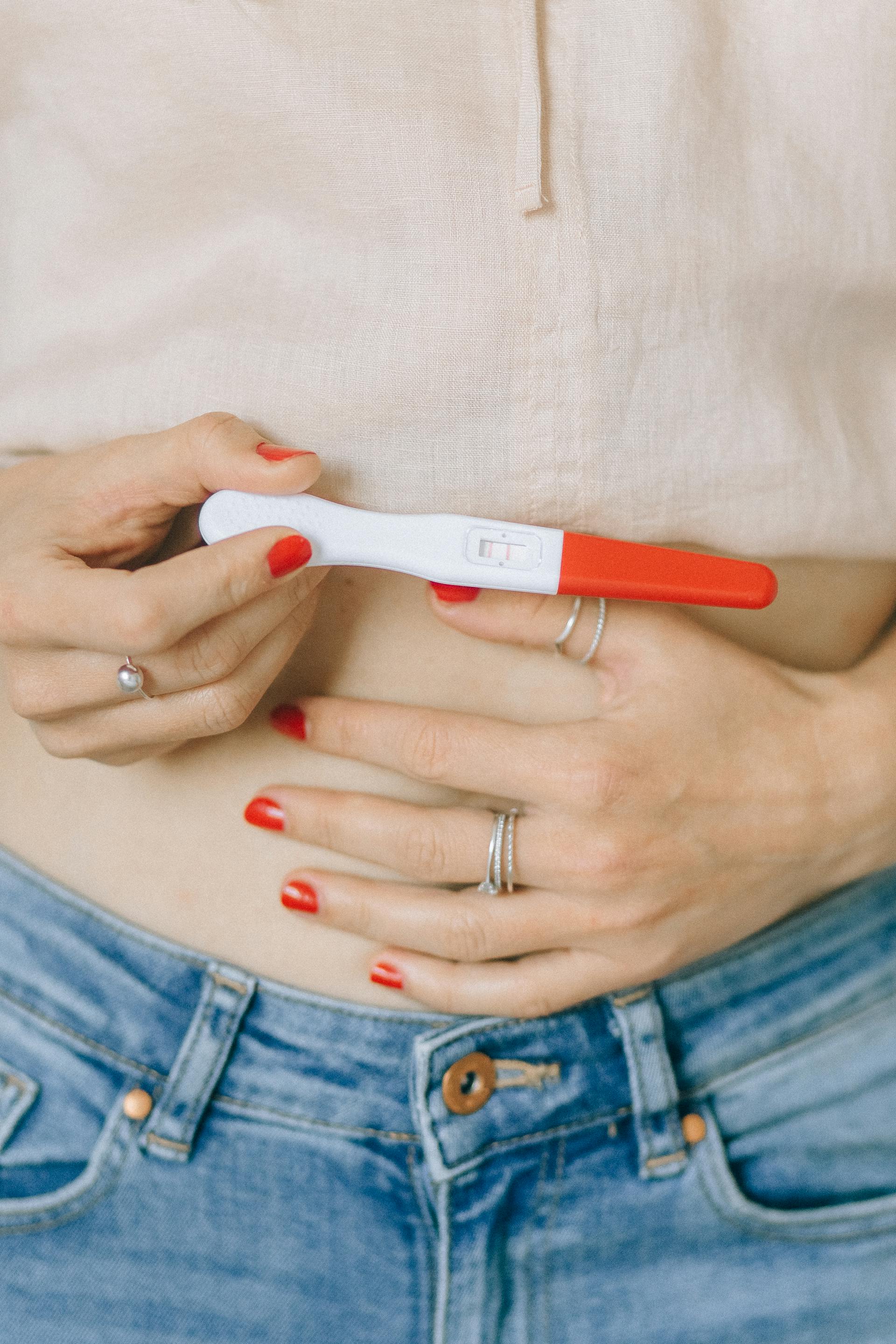 Close-up of a woman holding her belly and a pregnancy test kit | Source: Pexels