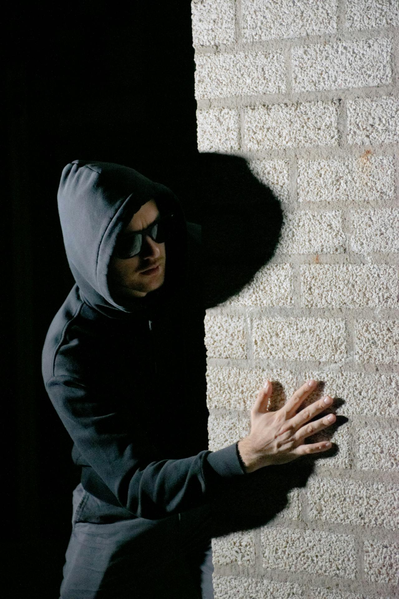 A suspicious man wearing hoodie and sunglasses standing behind a wall | Source: Pexels