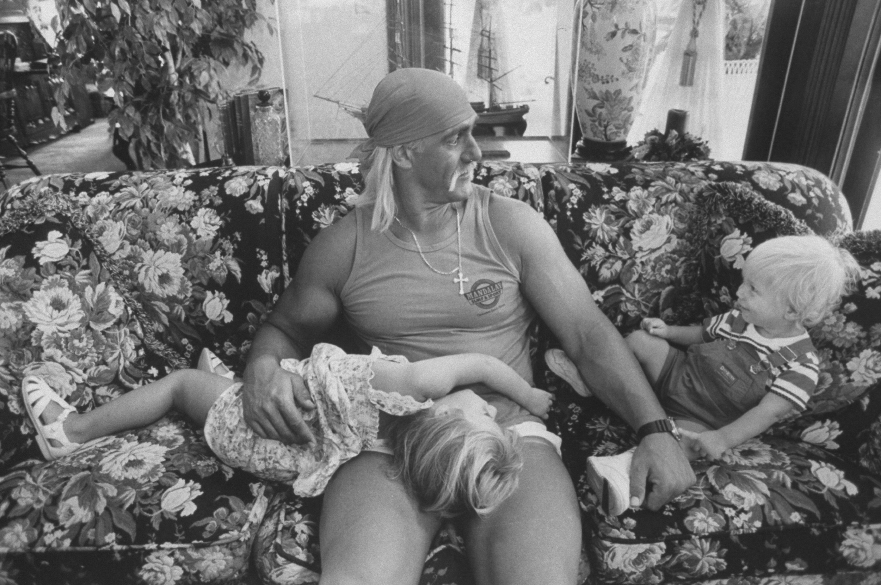 Wrestler Hulk Hogan cuddling w. his 3-yr-old daughter Brooke as he chats w. his 1-yr-old son Nicholas while relaxing together on a floral print couch at home, circa 1991. | Source: Getty Images