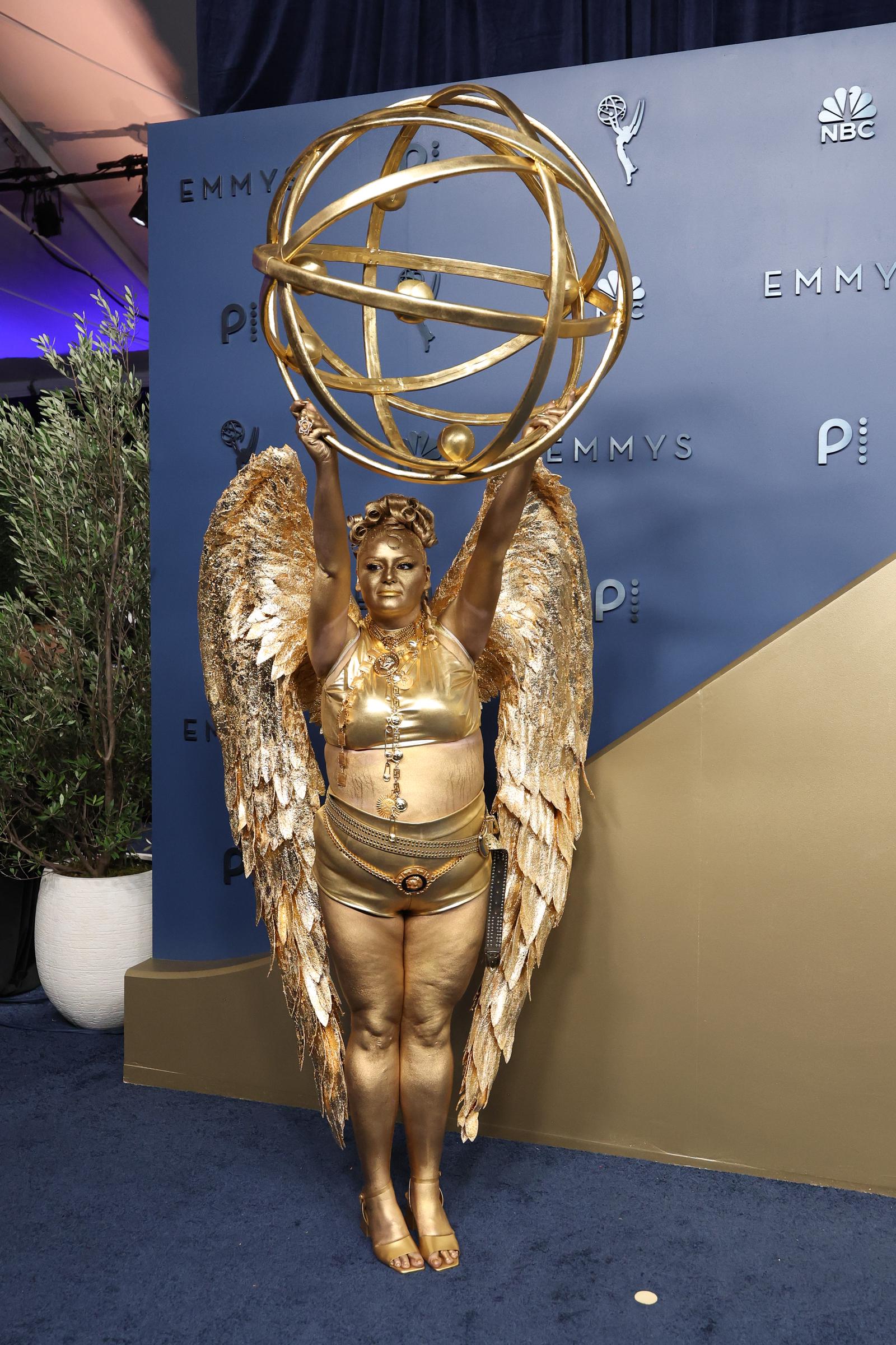 Meg Stalter poses in a head-to-toe gold ensemble with dramatic wings and an oversized Emmy statuette at the 78th Primetime Emmy Awards. | Source: Getty Images