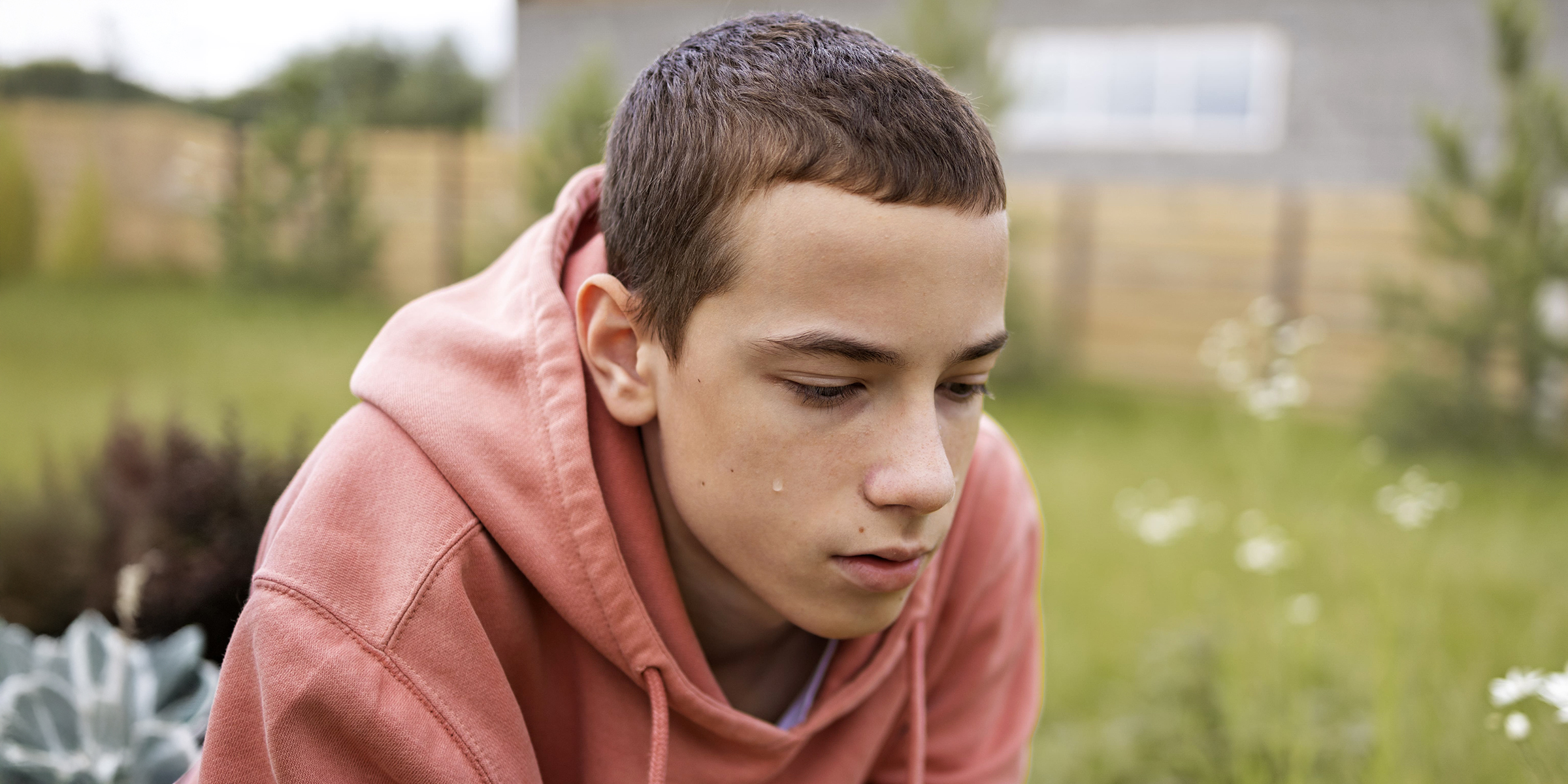 A depressed teenage boy sitting outdoor, his face downcast | Source: Freepik