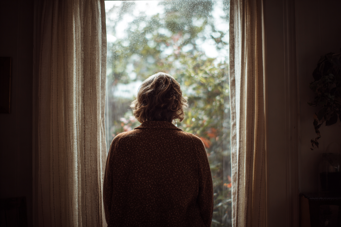 A woman looking outside a window | Source: Midjourney