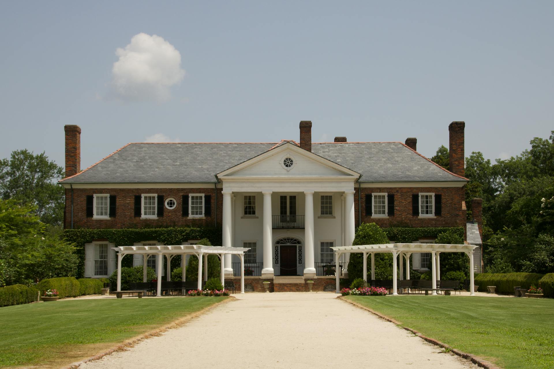 A two-story red brick mansion with a white portico and two white trellises on the front lawn | Source: Pexels