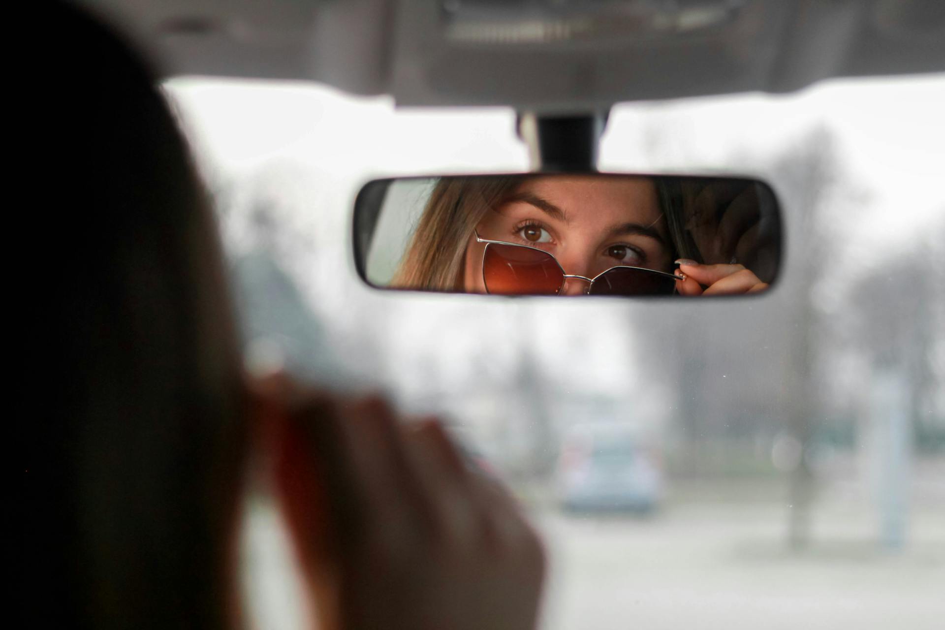 Confident woman in sunglasses looking at her reflection in the rearview mirror | Source: Pexels