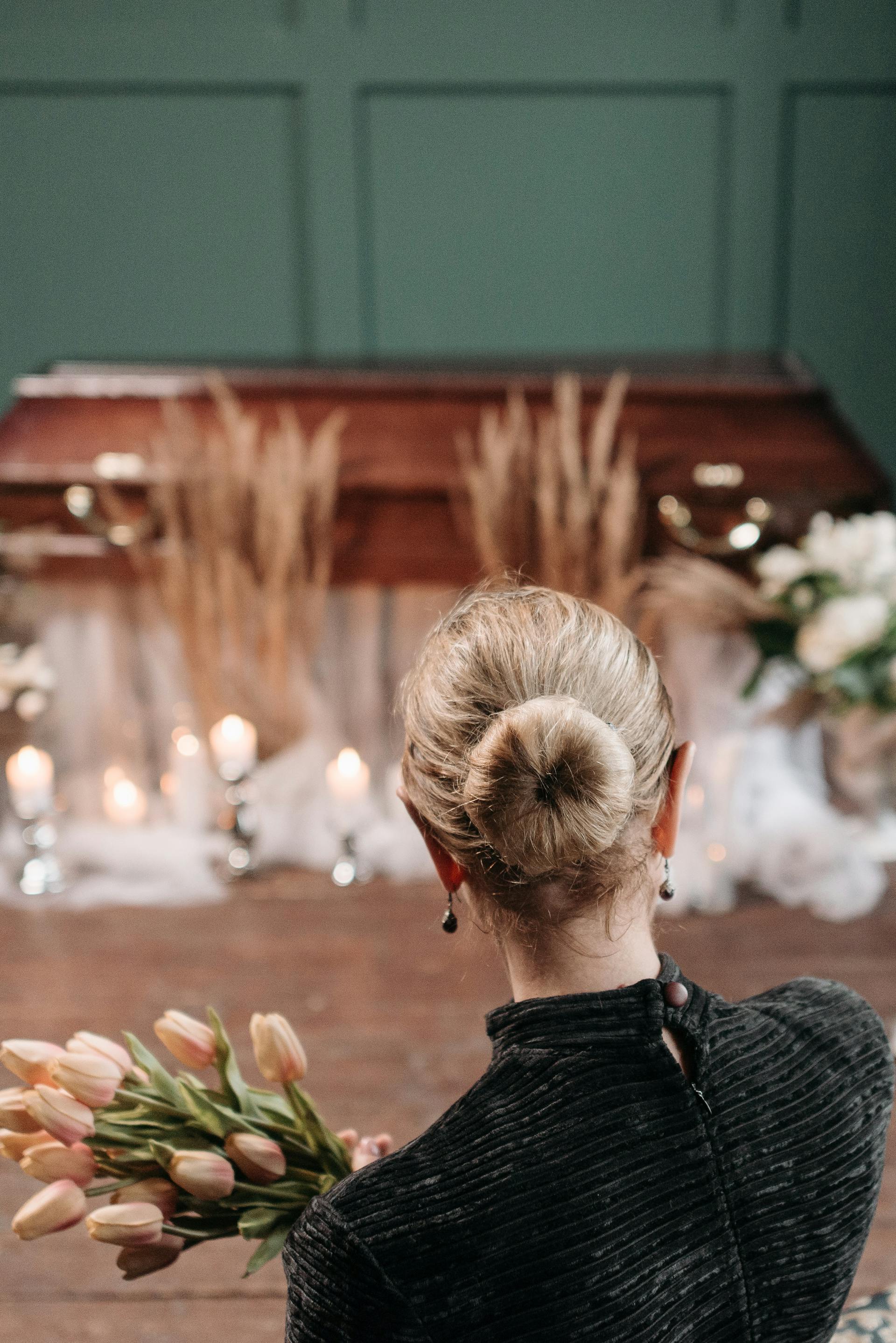 A woman holding a bouquet in front of a coffin | Source: Pexels